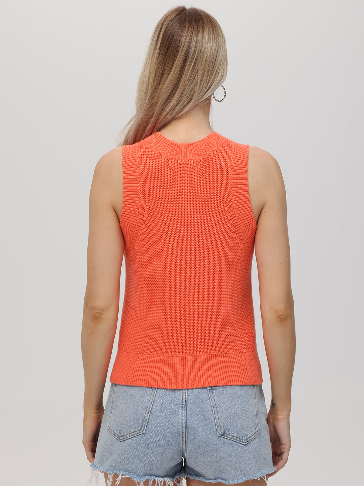 A person with long, light brown hair is seen from the back wearing a 525 America crew neck sleeveless orange knit top and frayed hem light blue denim shorts—a versatile look set against a plain light background.