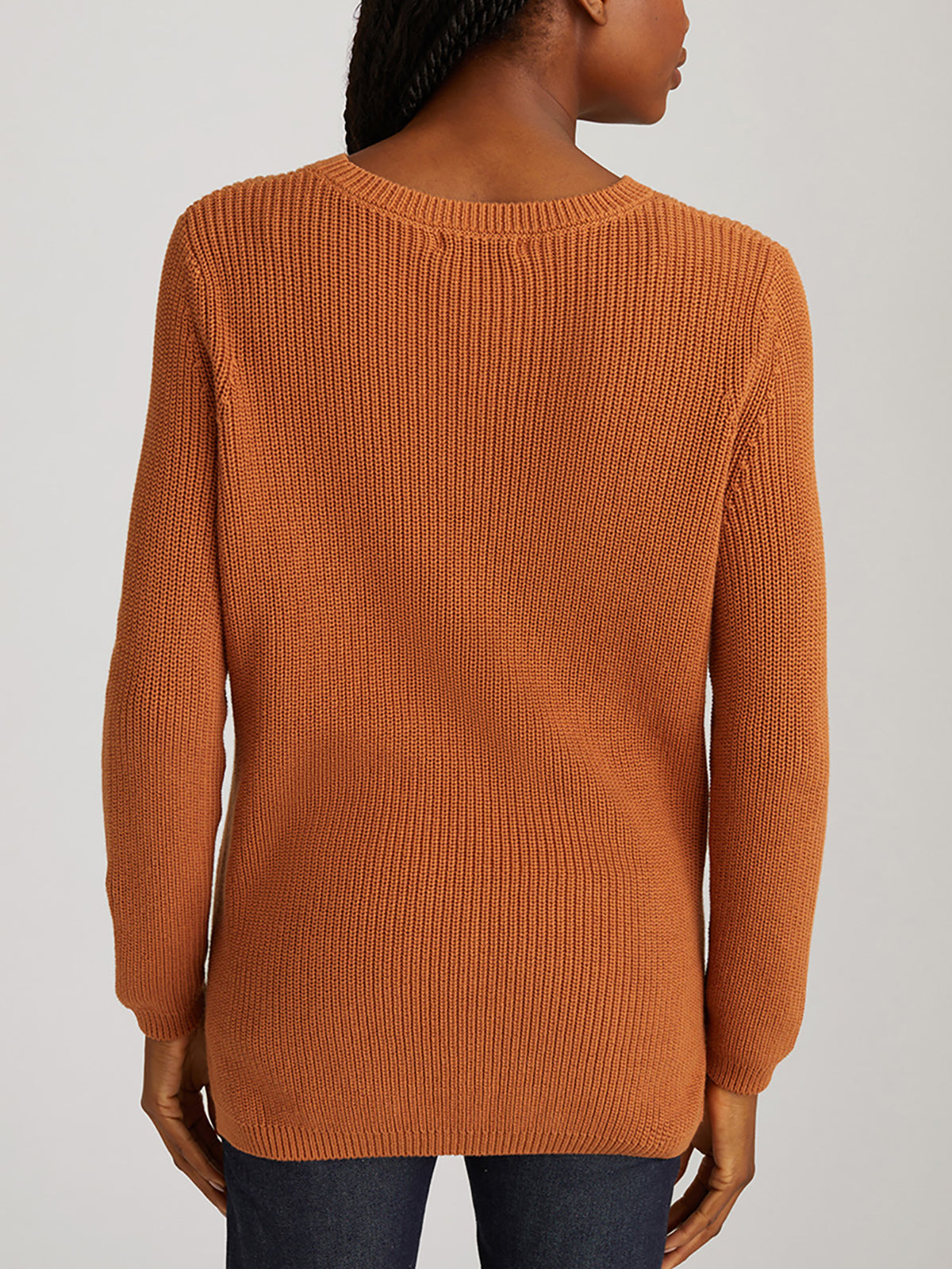 A person in a long-sleeved, ribbed brown 525 America sweater showcases its relaxed fit while standing with their back to the camera. Paired with dark jeans, this versatile style is set against a plain, neutral background.