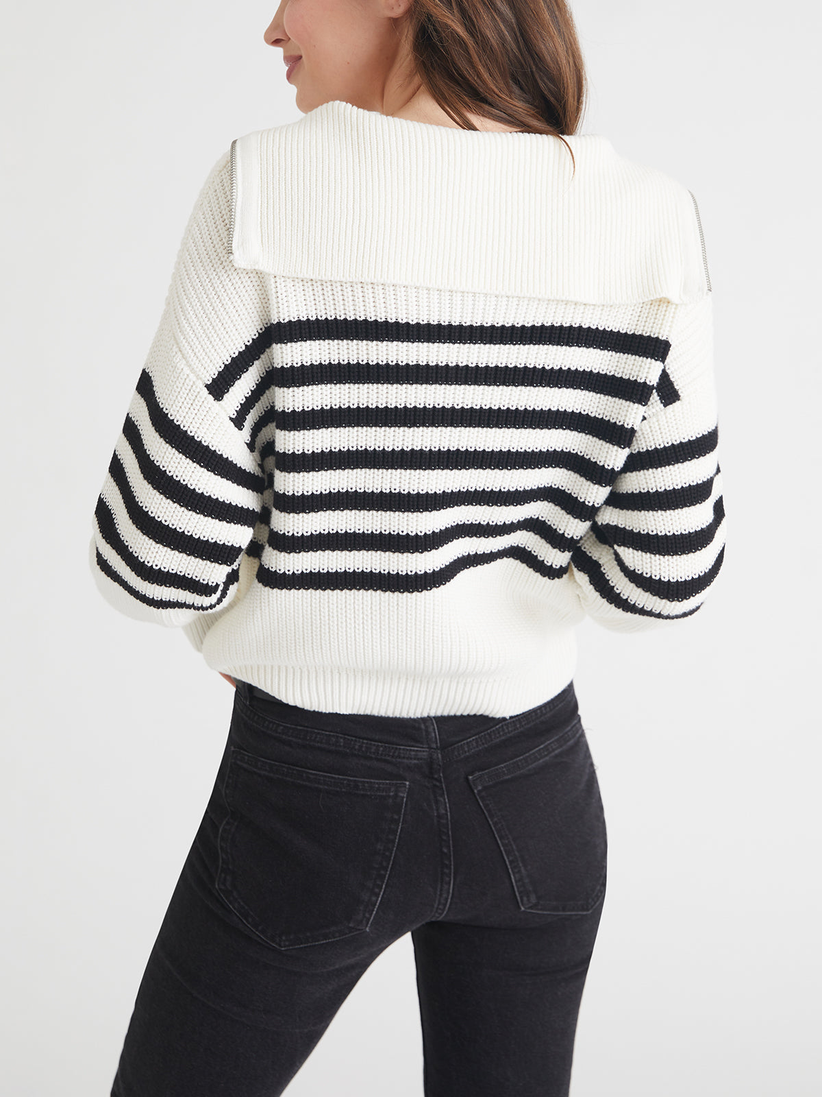 A person is seen from behind in a 525 America white sweater with black stripes and black jeans. The cotton sweater has a sailor-style collar and relaxed fit with dropped shoulders, set against a plain white backdrop.