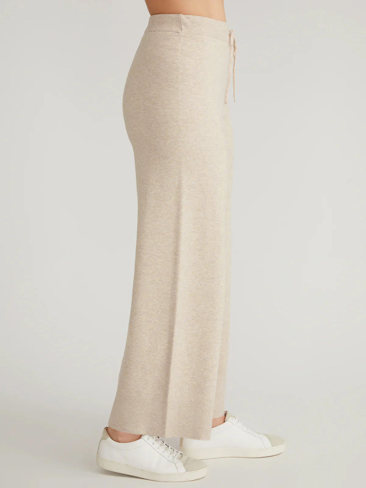 A person wearing a beige drawstring maxi skirt from 525 America and white sneakers, effortlessly paired with a cozy hooded knit sweatshirt. The plain background highlights the skirts soft fabric and the outfits casual elegance.