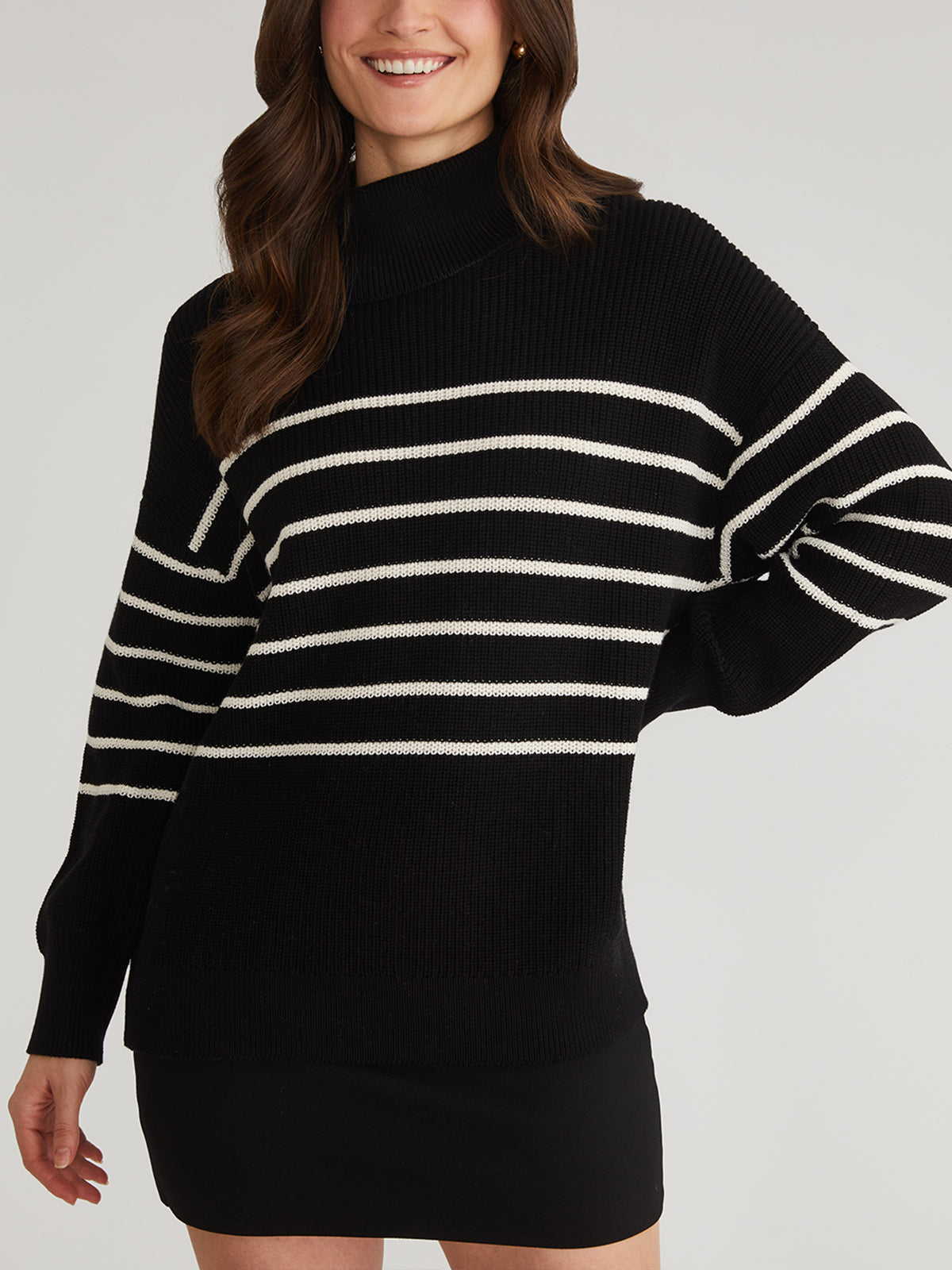 Someone is wearing a 525 America oversize stripe turtleneck pullover sweater with black and white horizontal stripes, paired with a black skirt. The sweater is 100% cotton, has long sleeves, a relaxed fit, and is set against a plain light-colored background.