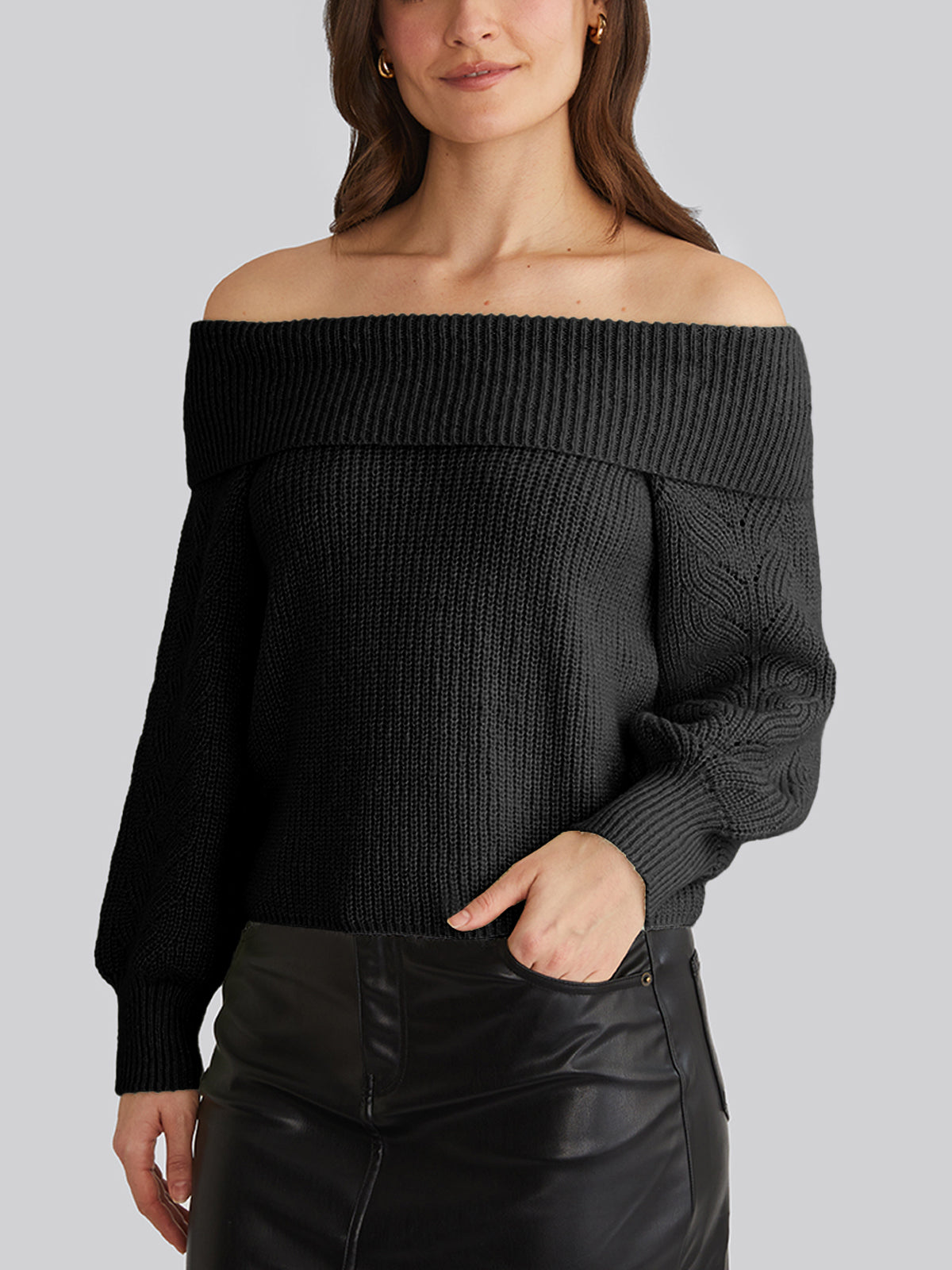 In a relaxed, off-the-shoulder pullover by 525 America, a woman exudes effortless chic. Pairing it with a black leather skirt, her long brown hair flows as she stands against a gray background. Her left hand rests confidently on her hip, embodying style perfect for casual outings.
