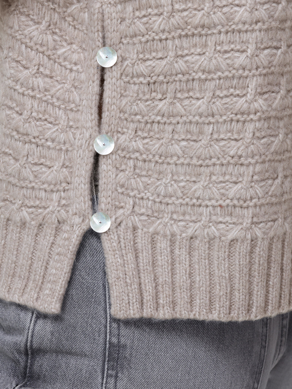 Close-up of the lower section of a 525 America beige knitted cardigan with button accents and a textured pattern, styled in a relaxed fit and worn over light gray denim jeans.