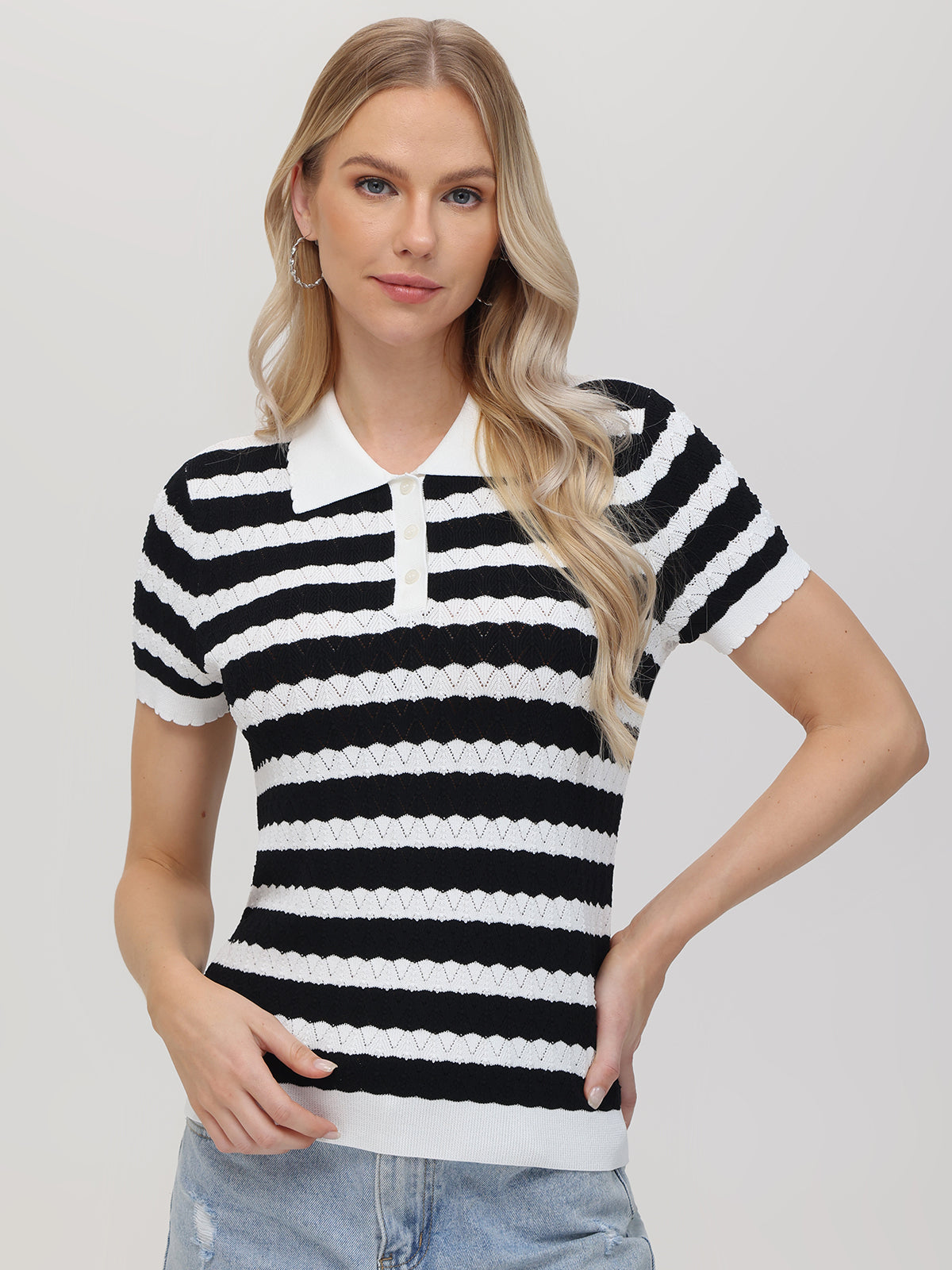 A person with long, blonde hair wears a 525 America black and white striped short-sleeve polo sweater featuring a white collar. They stand against a plain background in hoop earrings and light blue jeans, with one hand on their hip.
