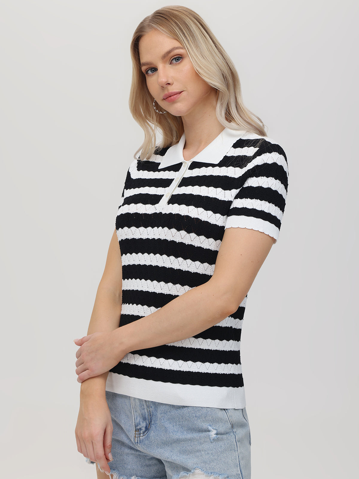 Someone with long blonde hair wears a black and white striped short-sleeve polo sweater by 525 America, paired with light blue distressed jeans, set against a plain light gray background.