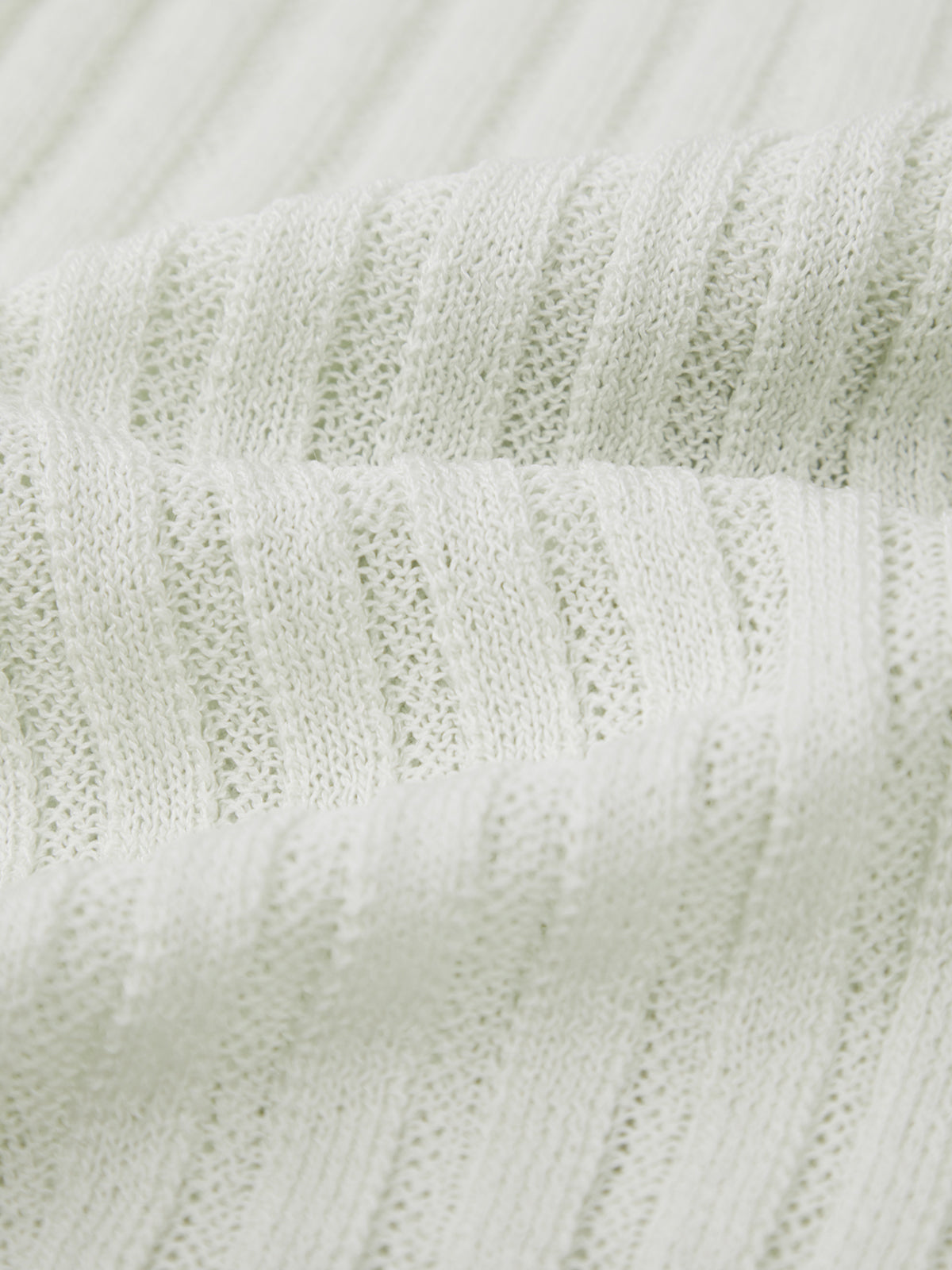 Close-up of a light-colored, ribbed sweater by 525 America. The soft fabric is shown in gentle folds, highlighting vertical ribbing and fine knit—perfect for pairing with a statement neckline.