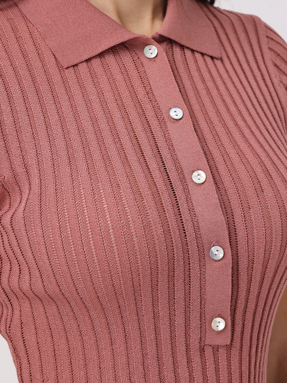Close-up of a person wearing a pink ribbed knit polo from 525 America. It features short sleeves, a statement neckline, classic collar, and button-up front with five white buttons. The fabric boasts textured vertical stripes for added style.