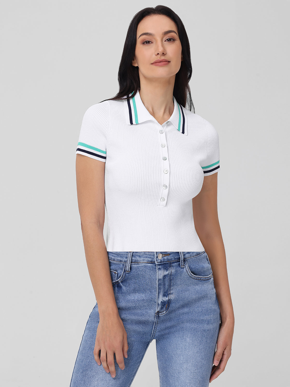 A person with long dark hair wears a 525 America white polo sweater with a striped johnny collar and sleeve bands, paired with high-waisted blue jeans, standing against a plain light gray background.