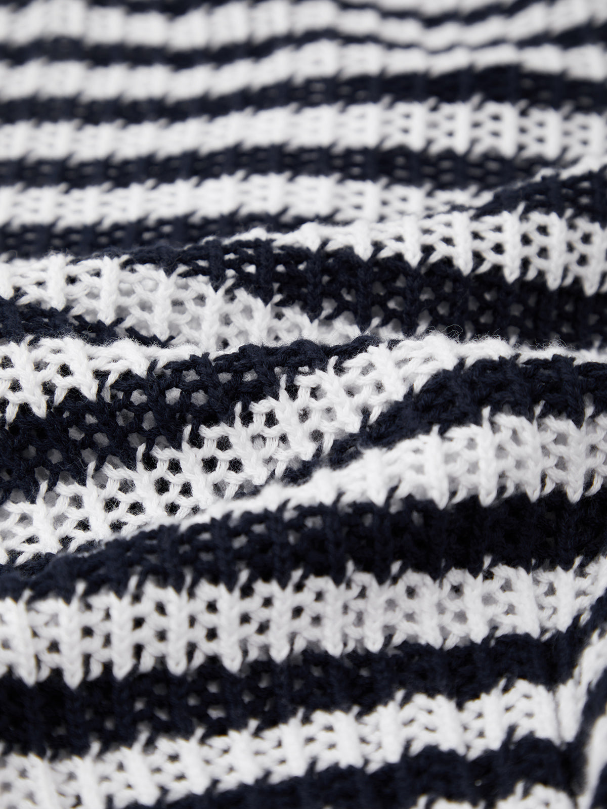 Close-up of a textured cotton sweater from 525 America with alternating navy blue and white stripes, featuring a grid-like open-weave knit for classic polo style.