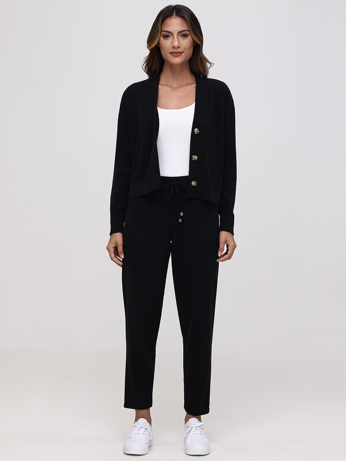 Against a plain backdrop, someone dons a black 525 America cardigan with button details, plush fabric drawstring pants, and white sneakers. A white top peeks from beneath the cardigan, creating a casual and comfortable look.