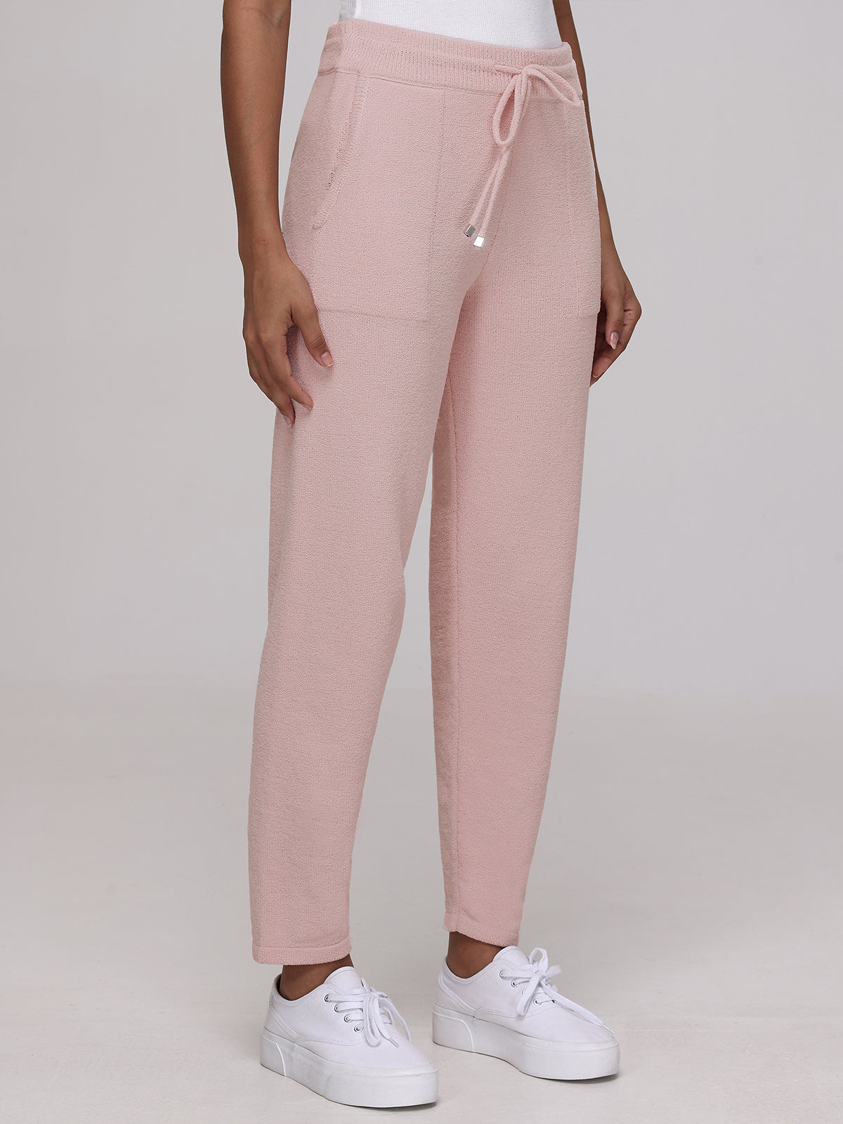 A person wearing 525 America light pink plush drawstring joggers with side pockets and white sneakers stands against a plain background, only the lower half visible.