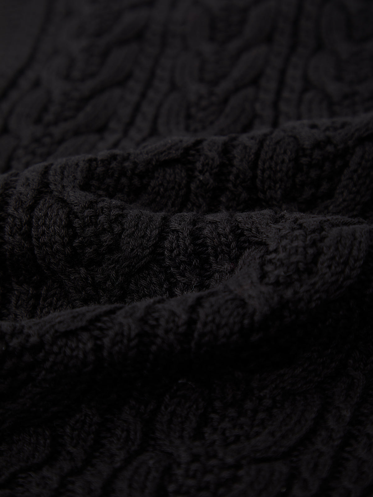 Close-up of a fitted black cable-knit fabric by 525 America, showcasing the textured pattern of intertwined yarns—ideal for layering.