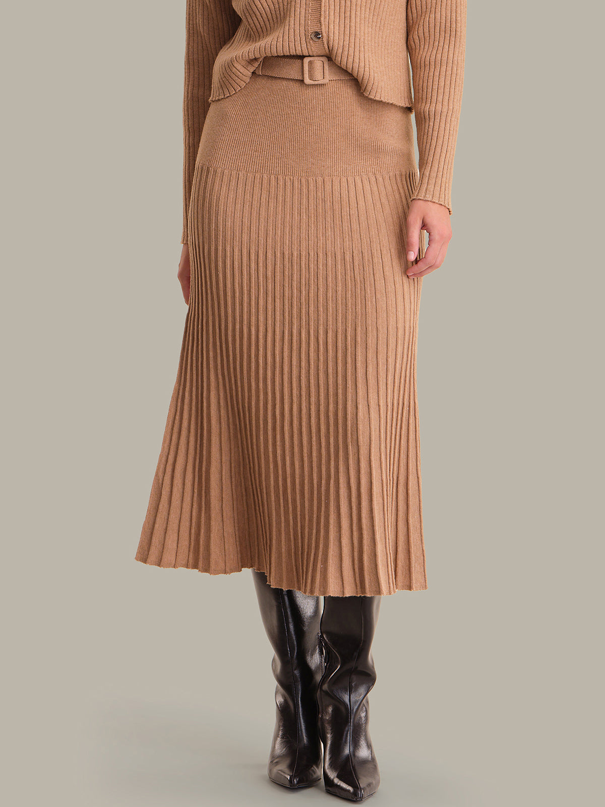Person wearing a brown ribbed sweater and skirt with black boots on a neutral background