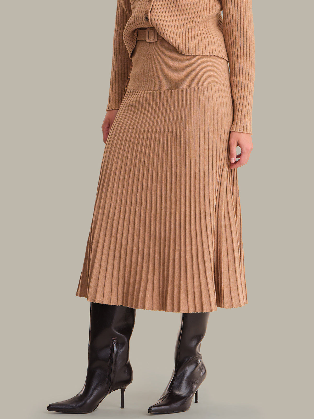 Person wearing a brown ribbed sweater and skirt with black knee-high boots on a neutral background