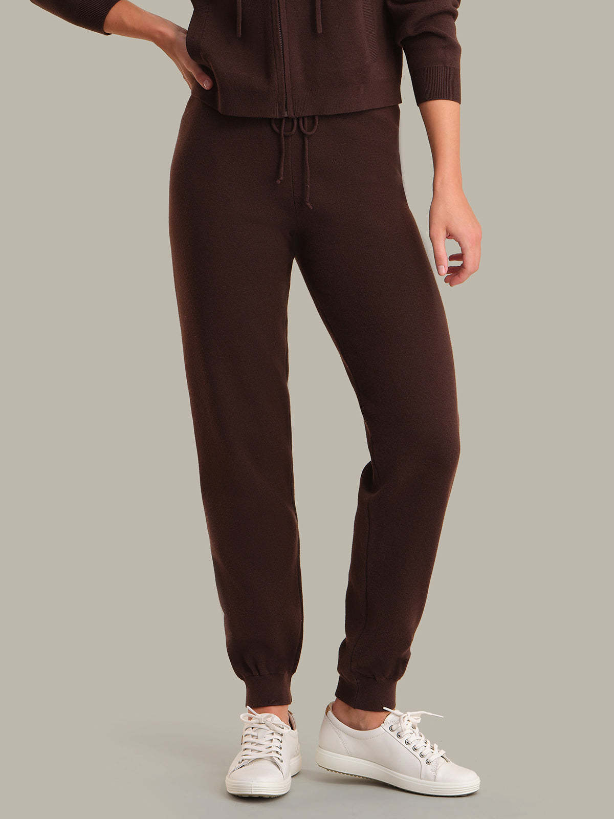 Person wearing brown sweatpants and a matching top on a gray background