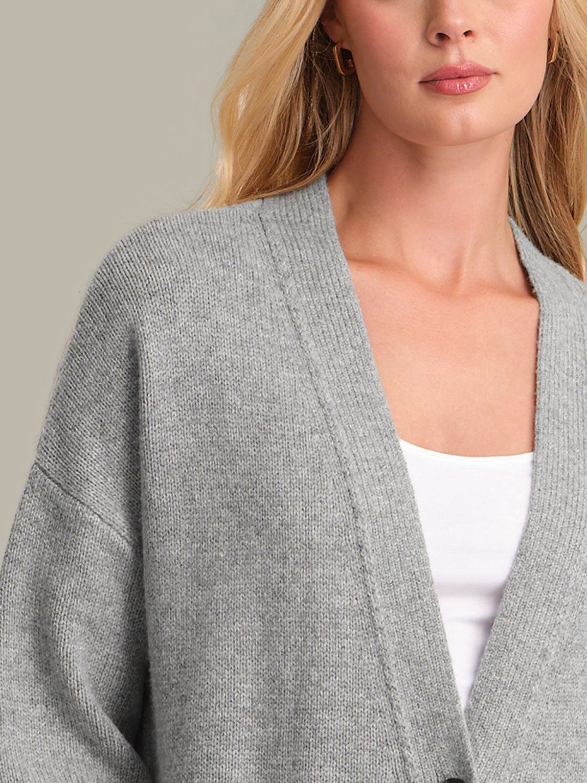 Woman wearing a gray cardigan over a white top against a neutral background