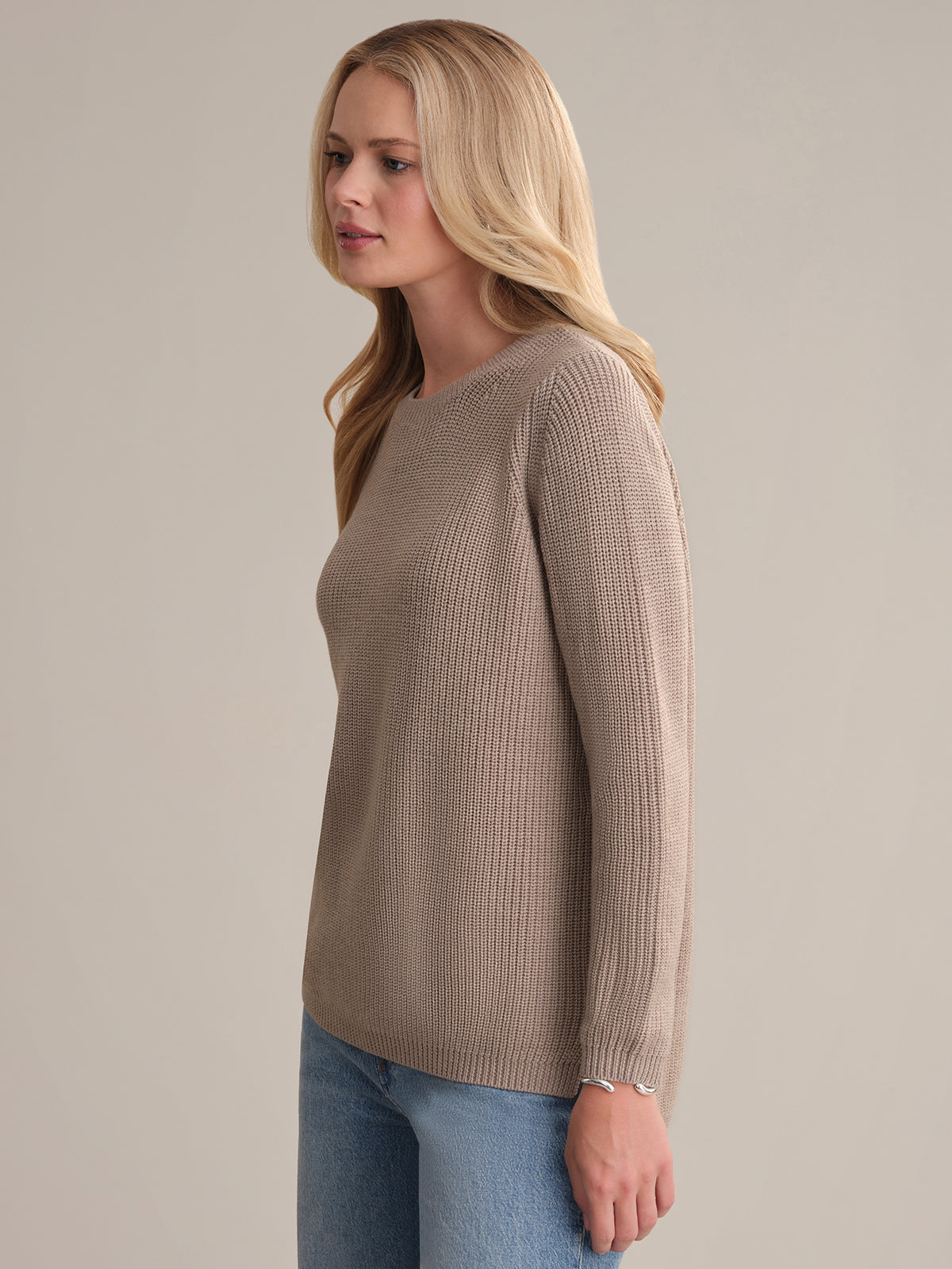 Woman wearing a beige sweater and blue jeans against a plain background