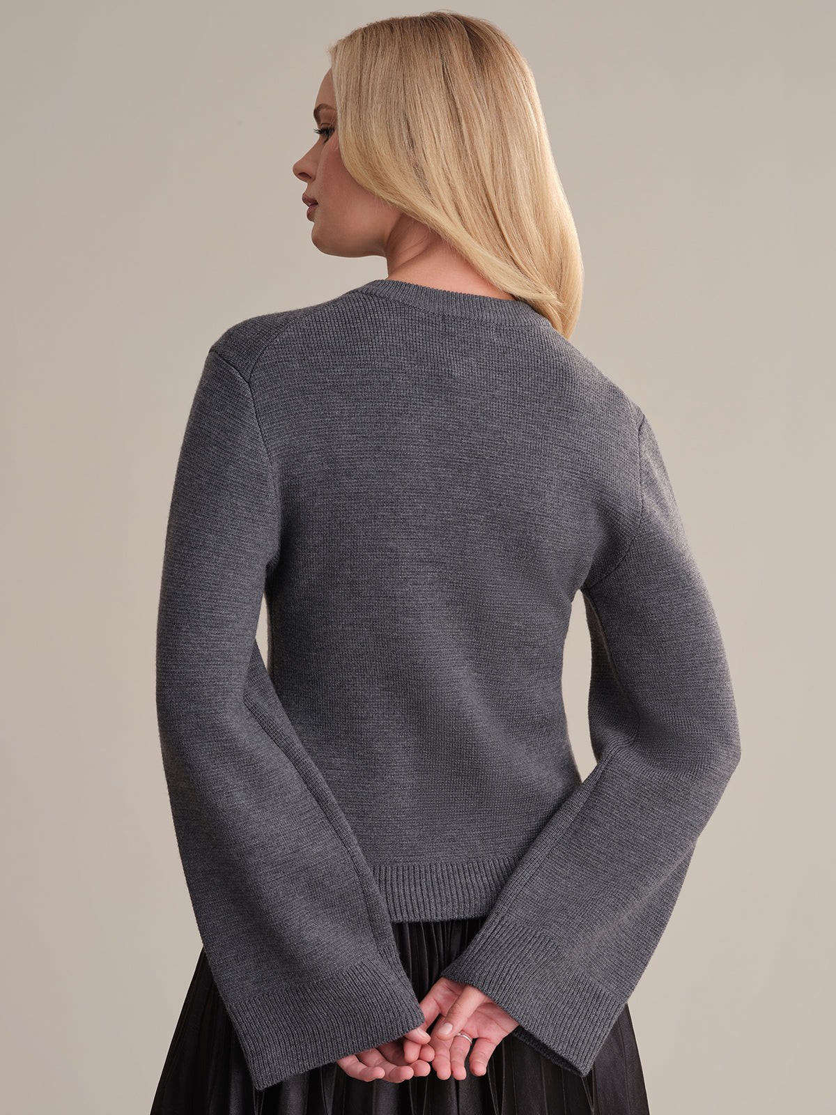 A person with long blonde hair stands, turned slightly left, wearing the elegant Catherine Wool Cardigan with flared sleeves against a plain, neutral background.