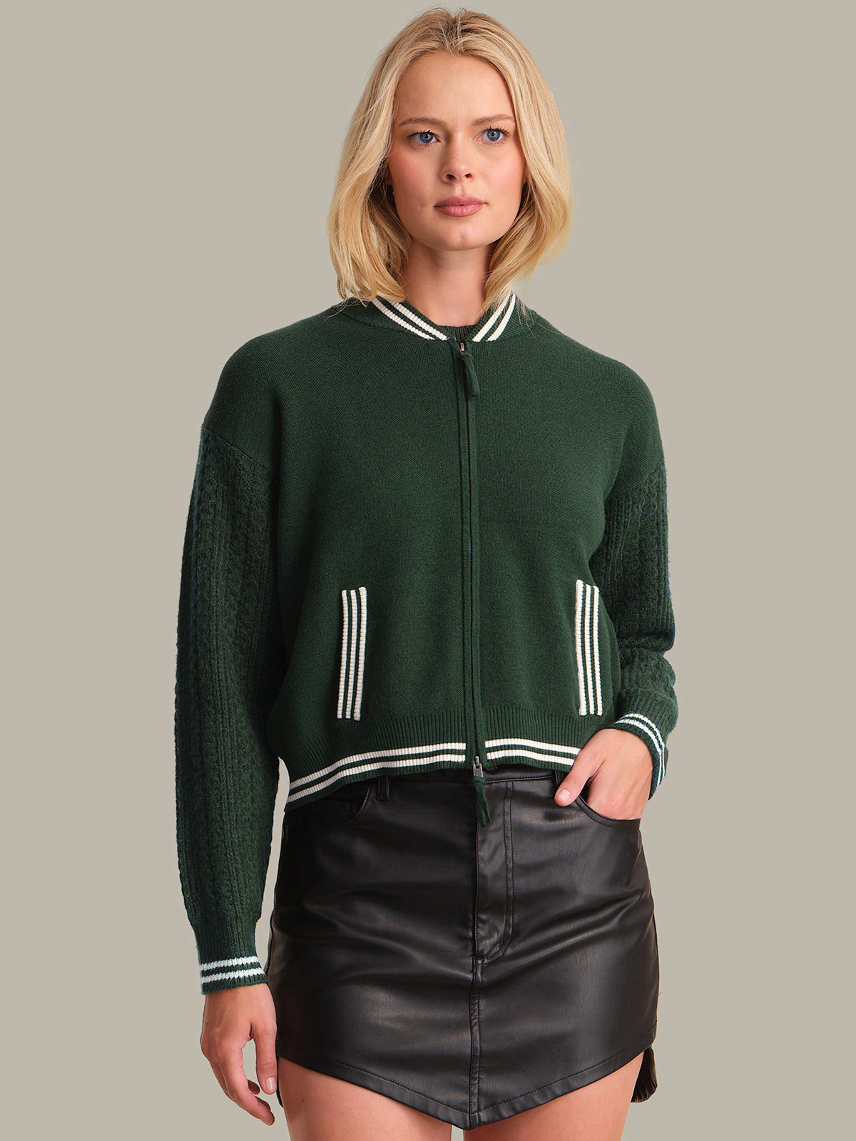 Woman wearing a green jacket with white trim and a black leather skirt on a gray background