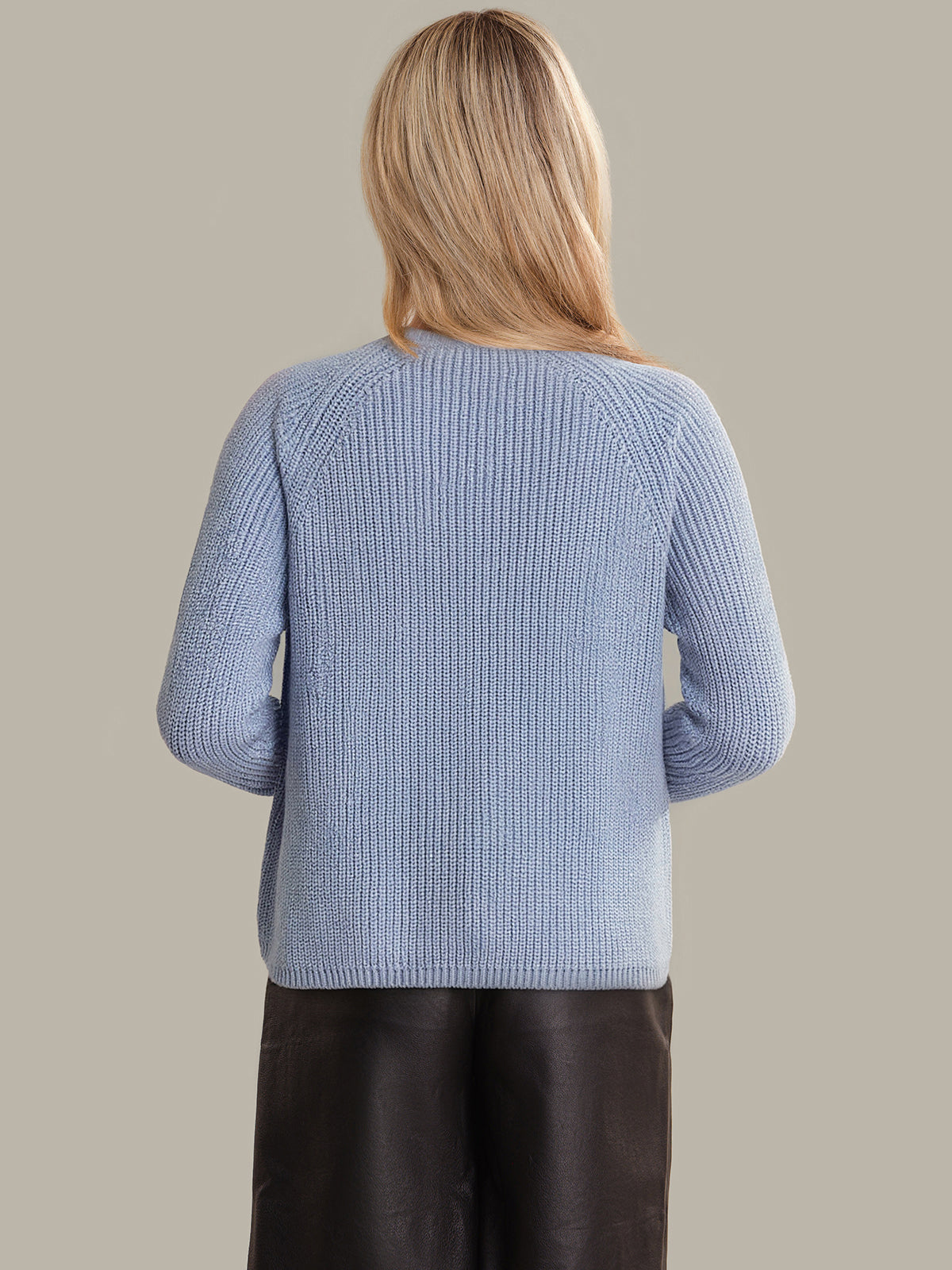 Person wearing a light blue knitted sweater on a beige background