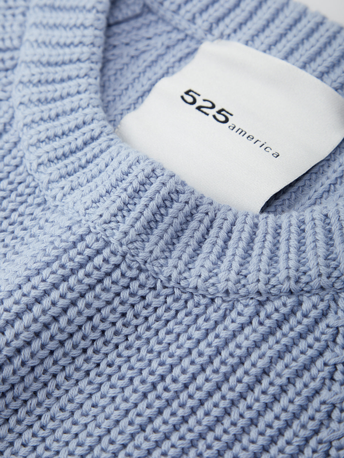 Close-up of a blue knitted sweater with a white label displaying '525 america'.