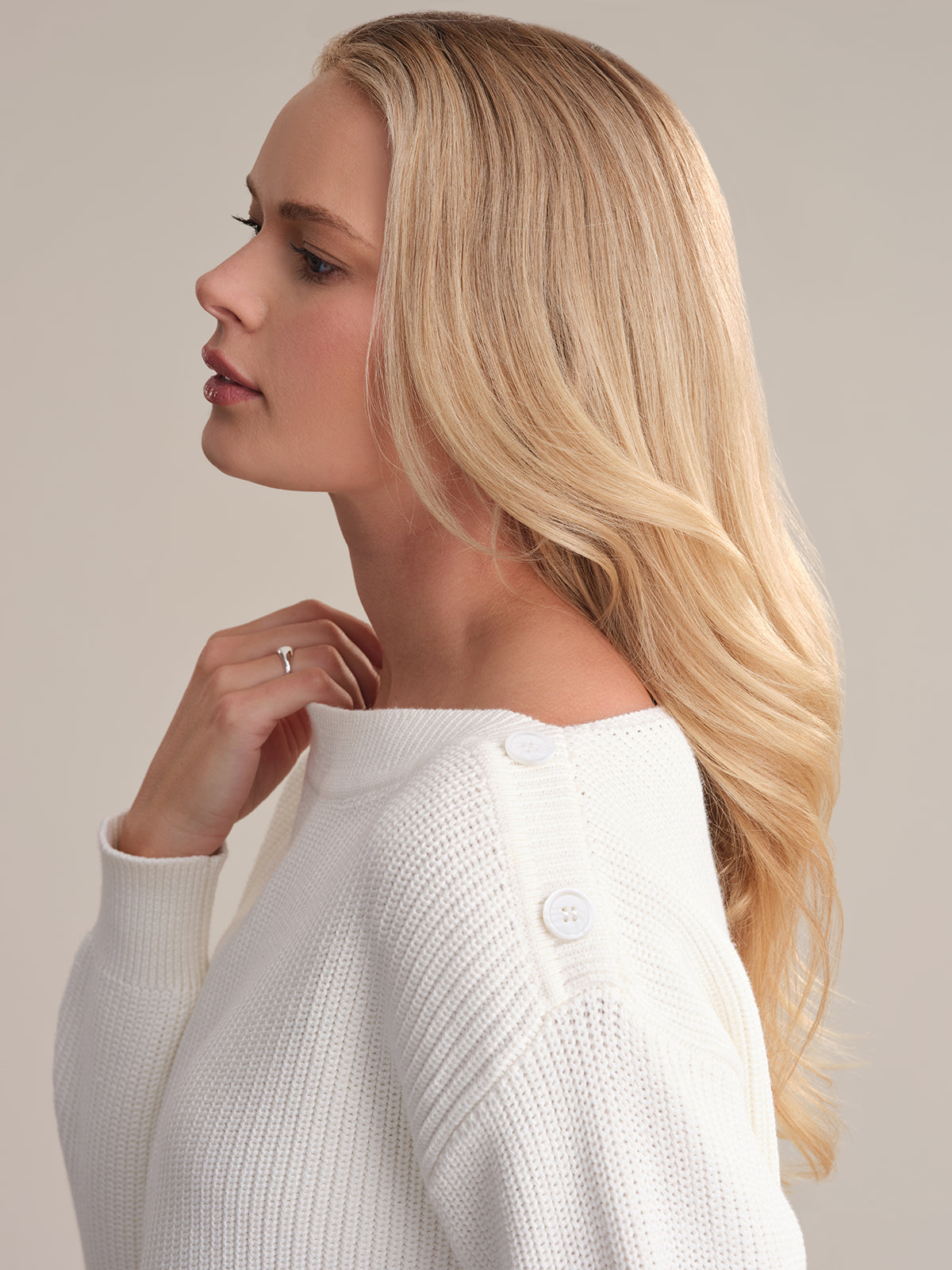A person with long, blonde hair appears in profile, showcasing a 525 America sweater with a boat neck and shoulder button details. Their hand is near their neck, emphasizing the garments elegance against a neutral background.