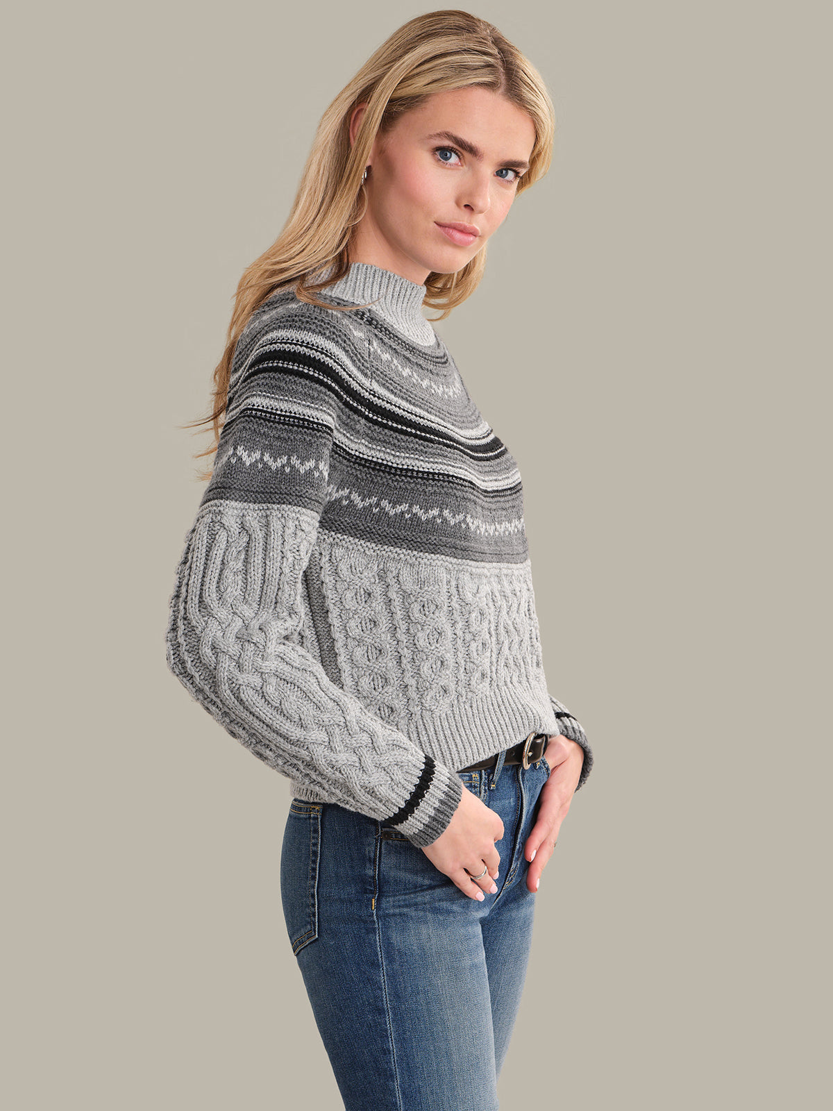 Woman wearing a gray patterned sweater and blue jeans on a beige background