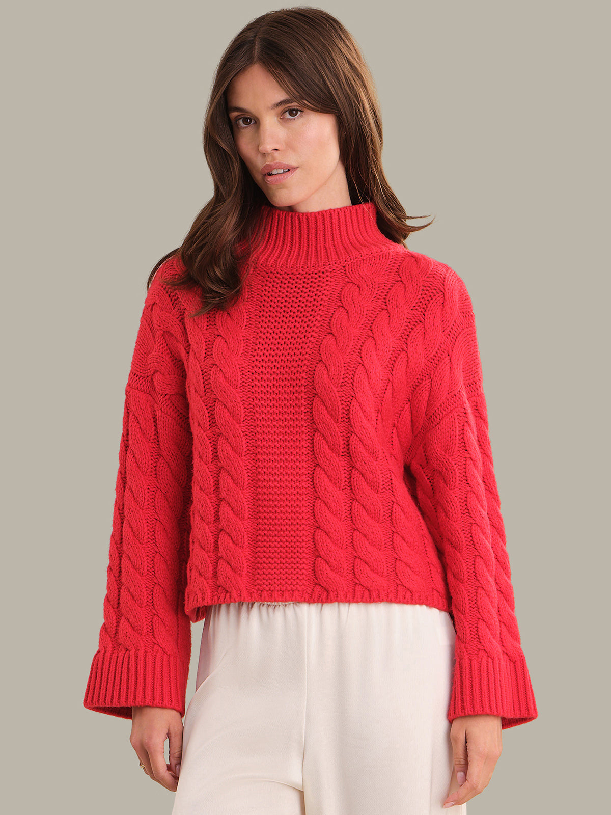 Woman wearing a red cable knit sweater against a neutral background
