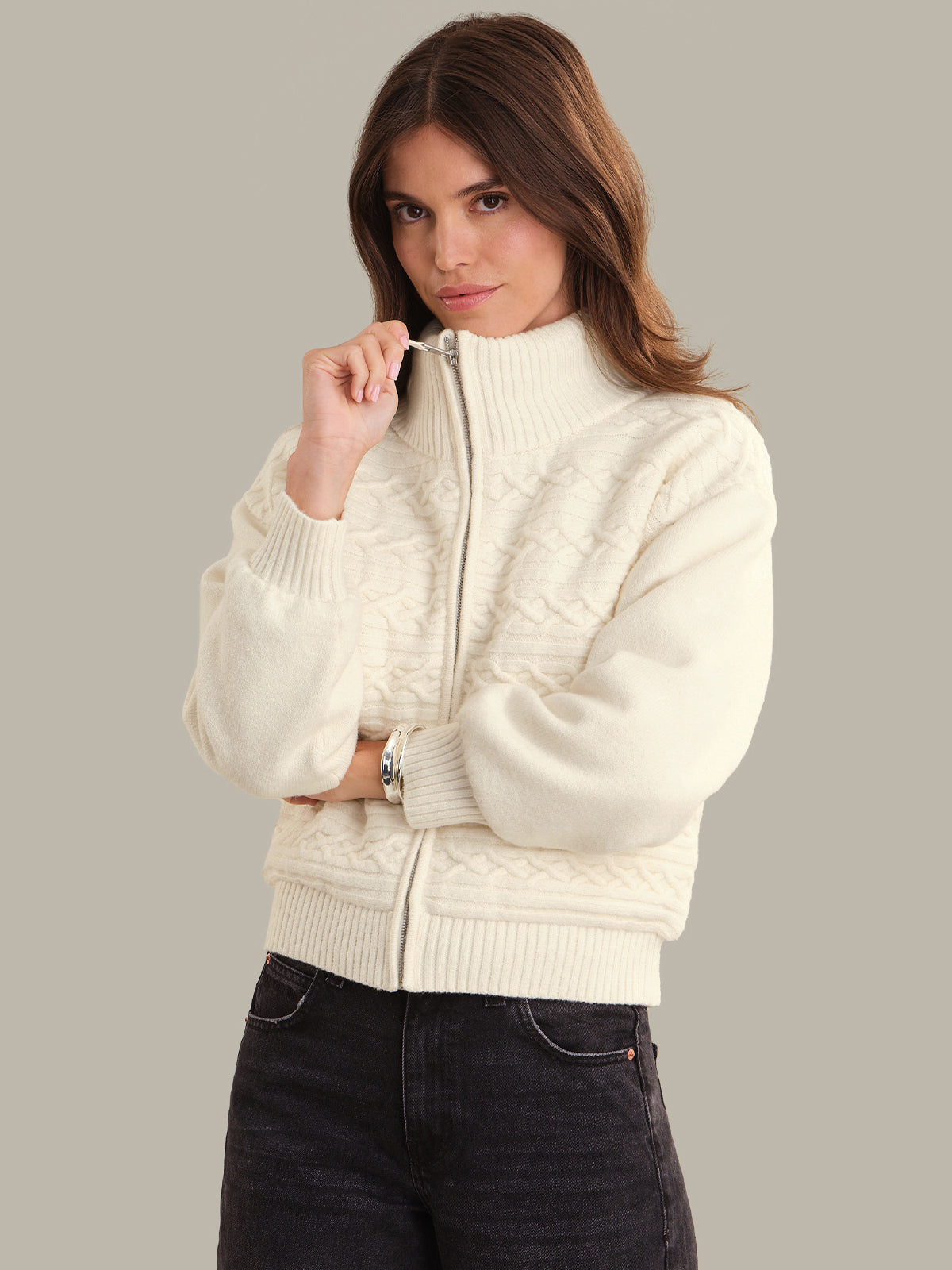 Woman wearing a cream-colored zip-up sweater jacket against a plain background