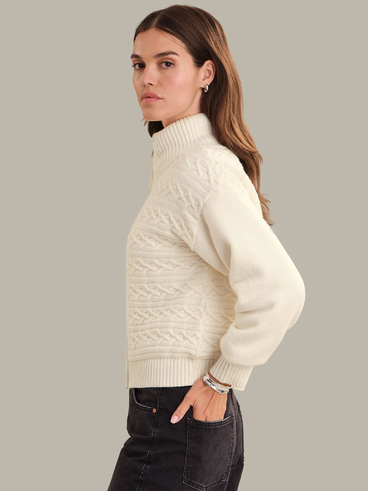 Woman wearing a cream cable knit sweater jacket against a plain background