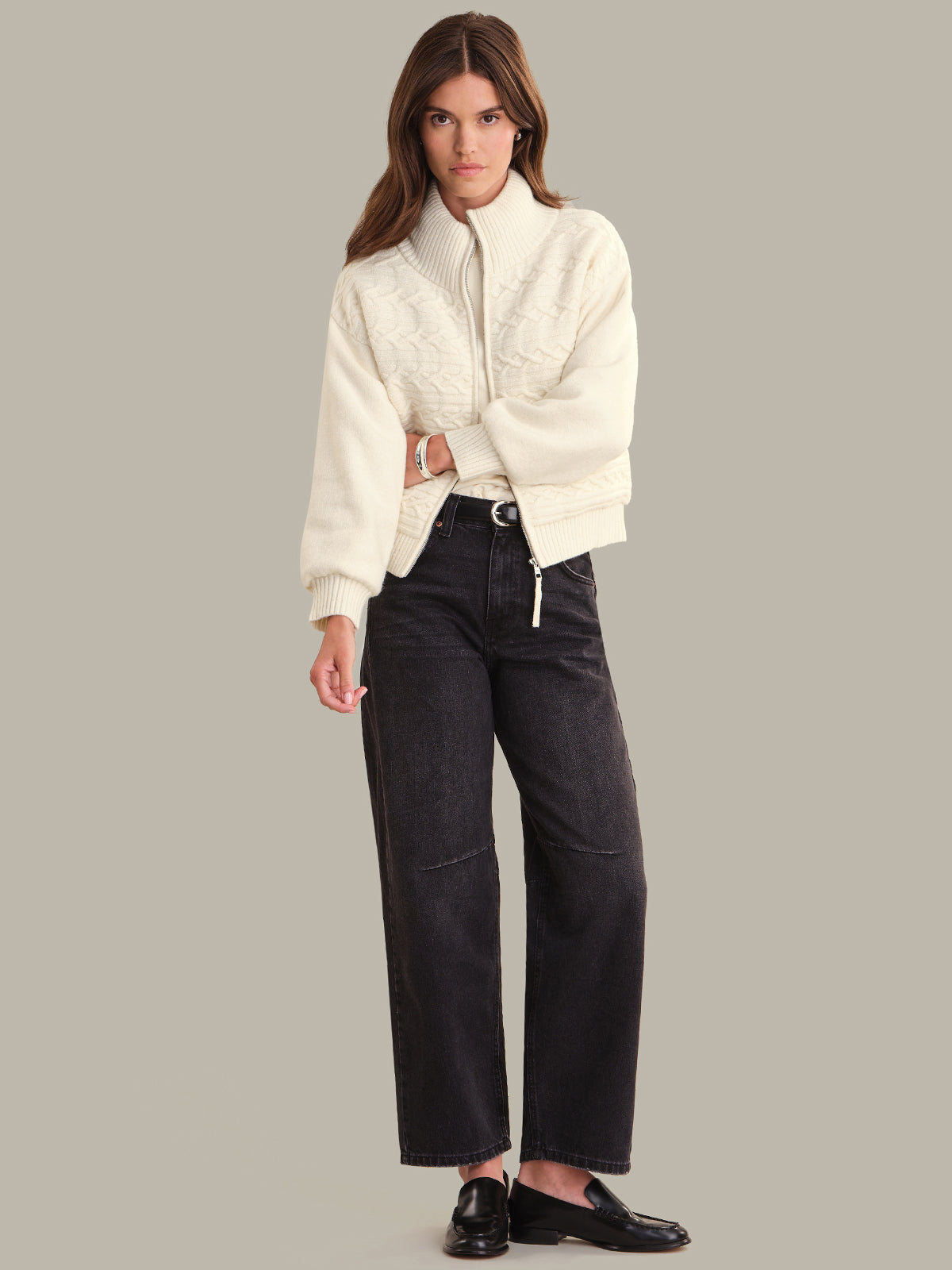 Woman wearing a white sweater jacket and black pants on a gray background