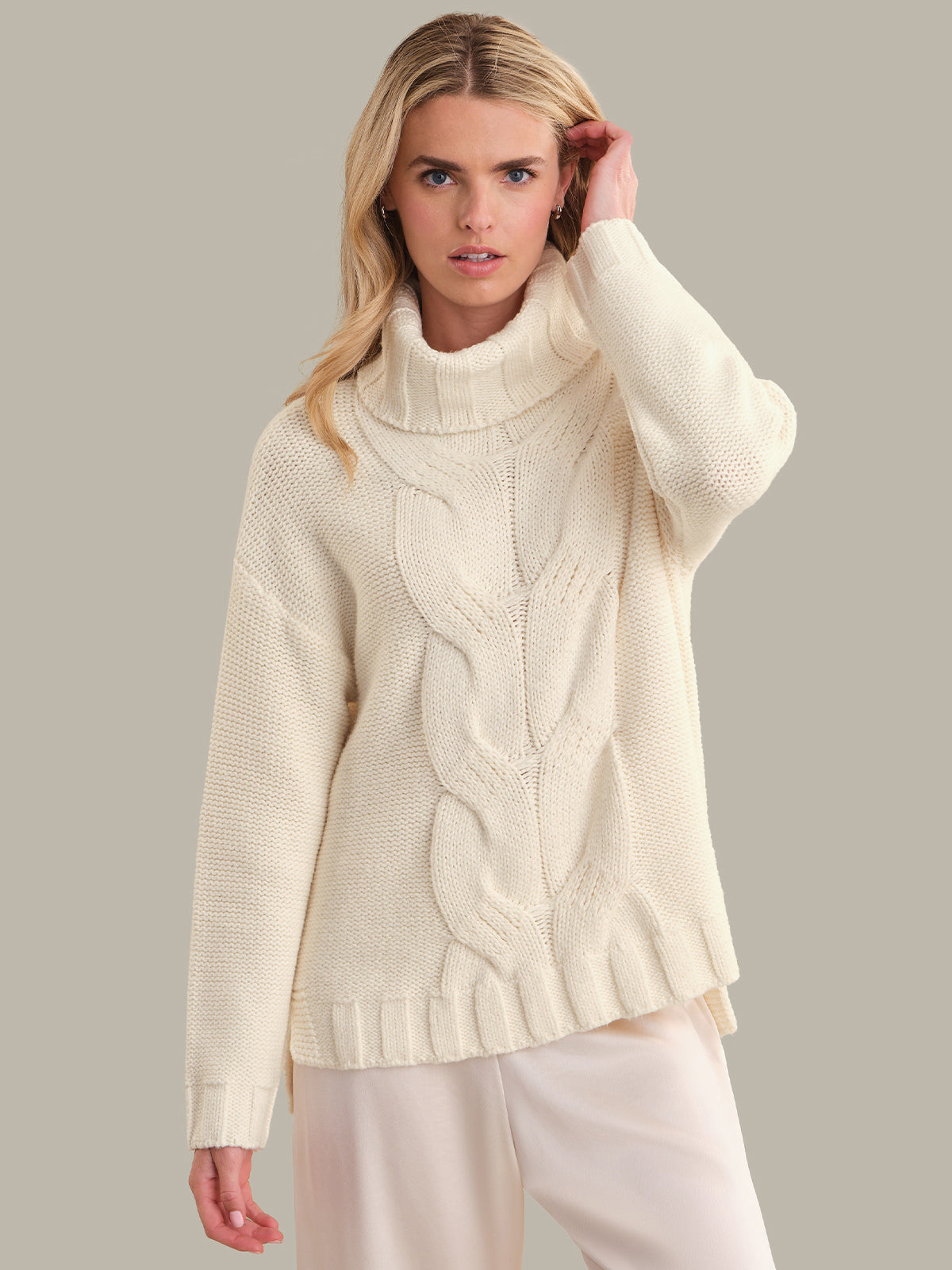 Woman wearing a cream cable knit sweater against a plain background