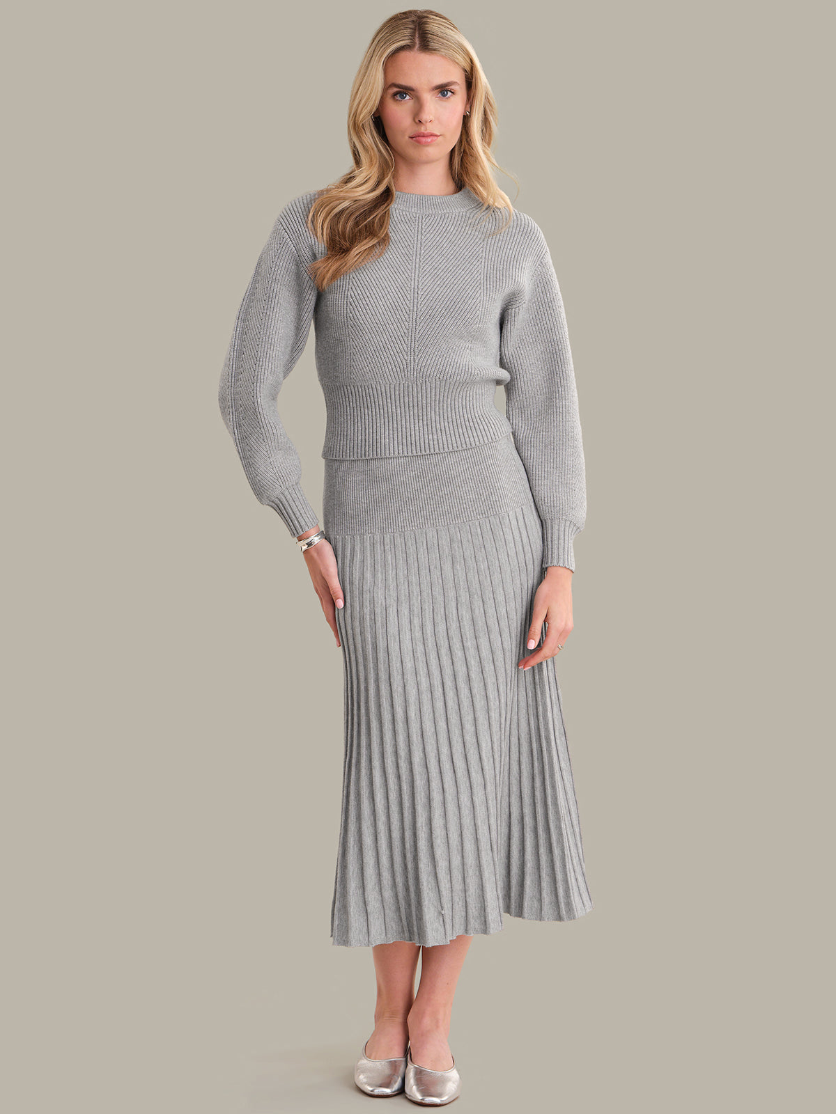 Woman wearing a gray ribbed sweater and skirt set against a plain background