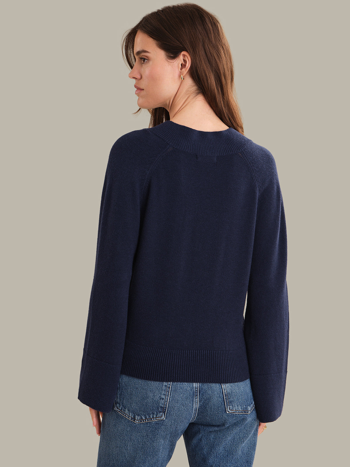 Woman wearing a navy sweater and blue jeans on a plain background