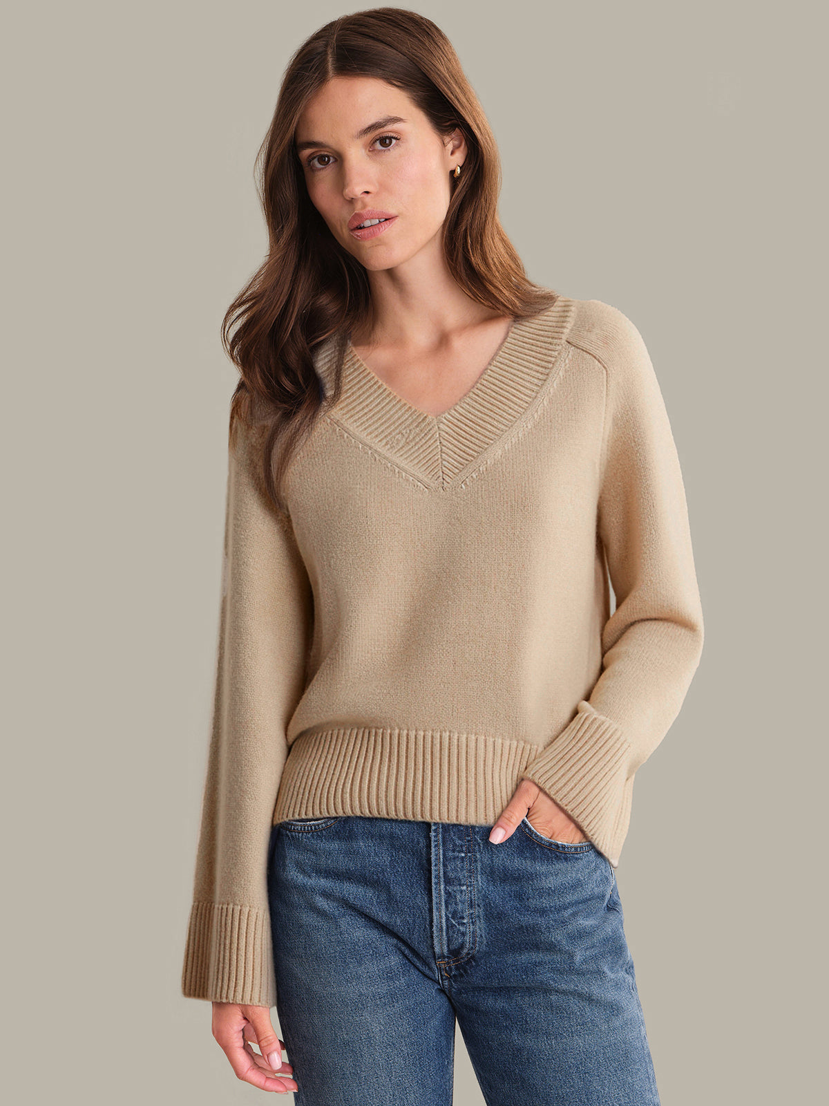 Woman wearing a beige sweater and blue jeans on a neutral background
