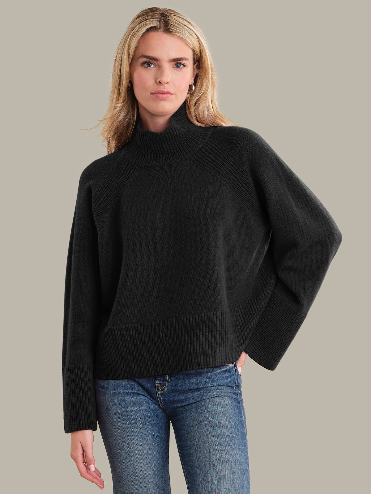 Woman wearing a black sweater and blue jeans on a beige background