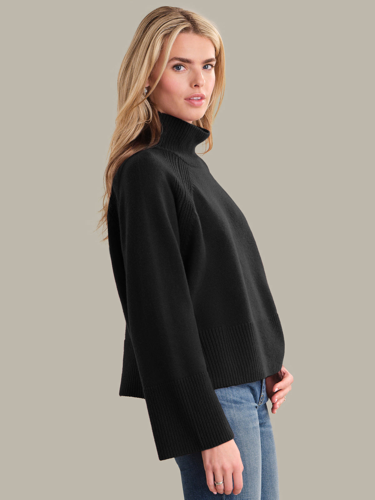Woman wearing a black turtleneck sweater and blue jeans on a gray background
