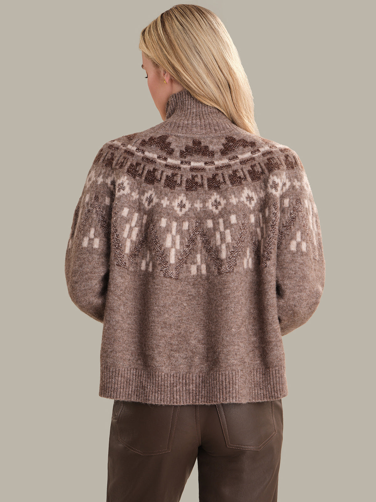 Person wearing a brown knitted sweater with a pattern on a plain background