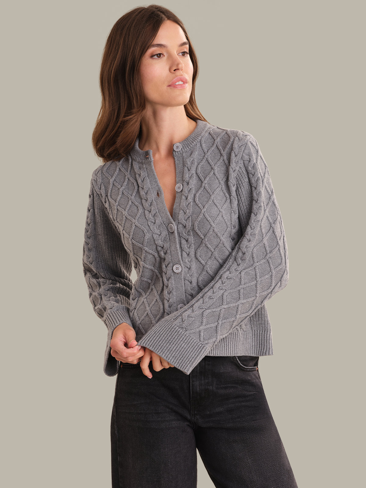 Woman wearing a gray cable knit cardigan against a plain background