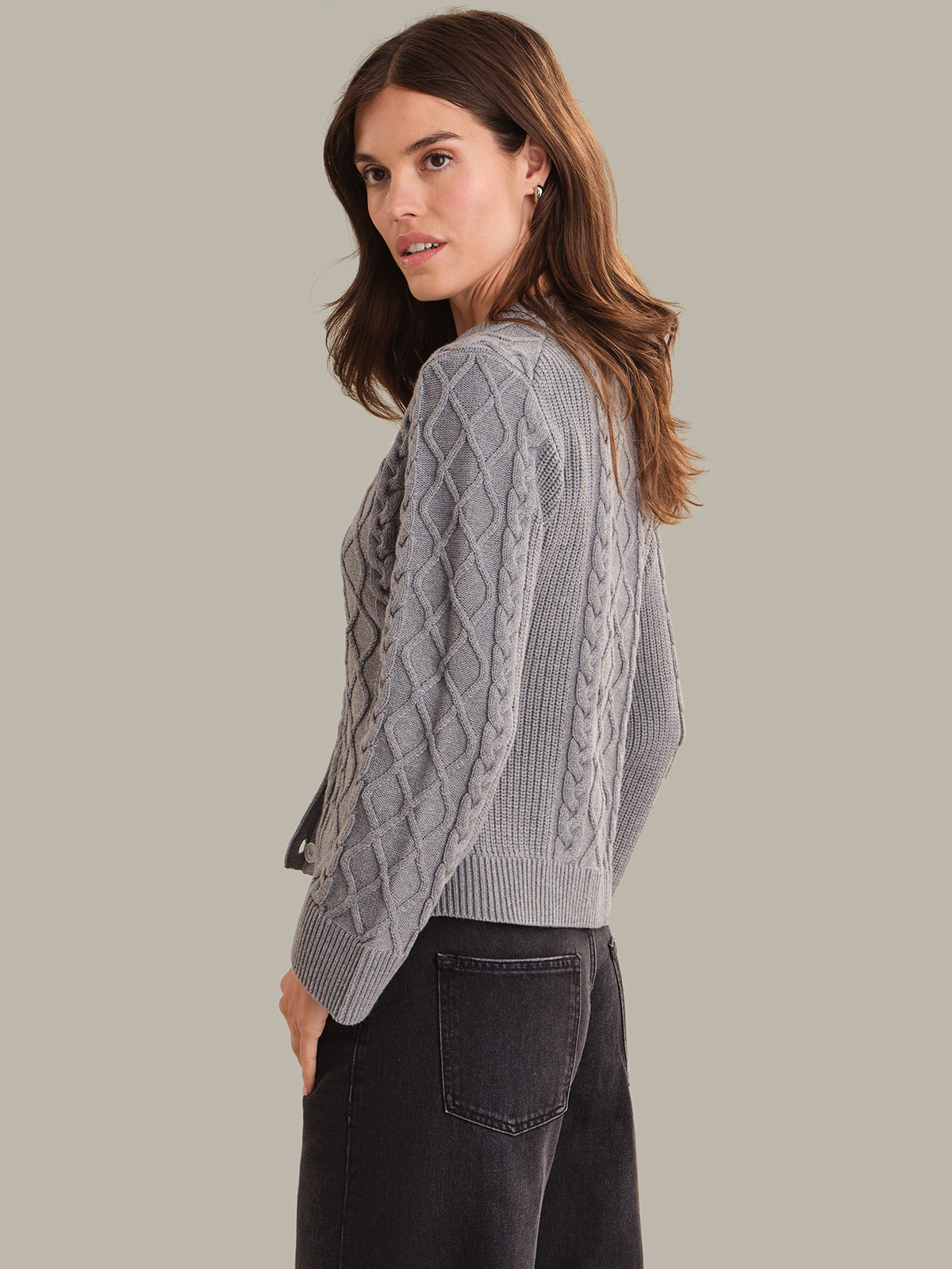 Woman wearing a gray cable knit sweater against a plain background
