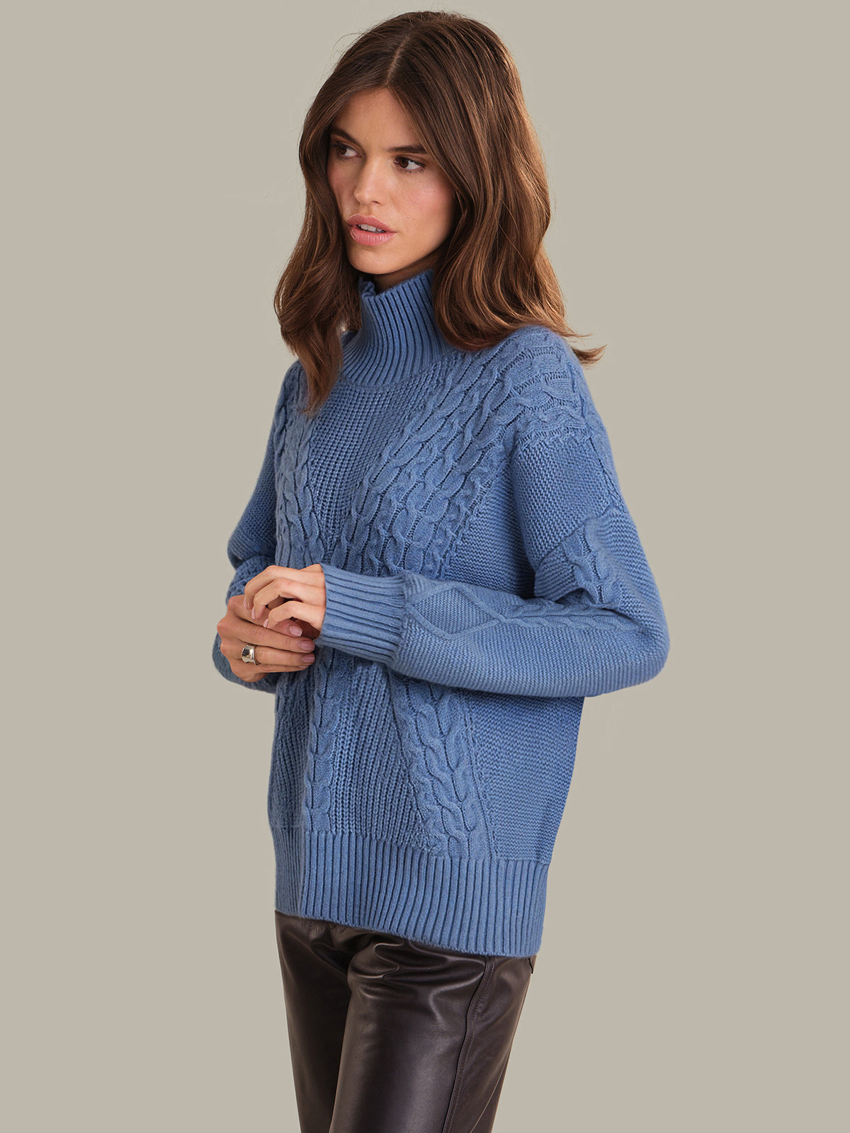 Woman wearing a blue cable knit sweater against a neutral background