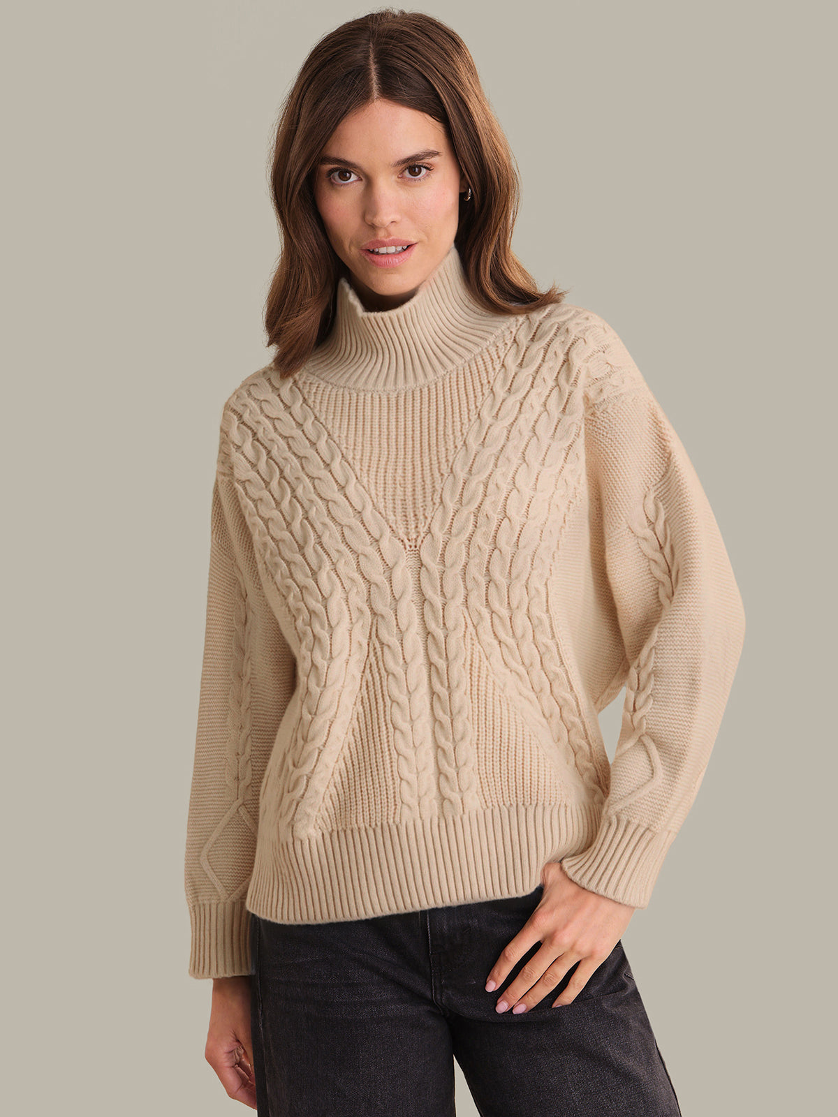 Woman wearing a beige cable knit sweater against a plain background
