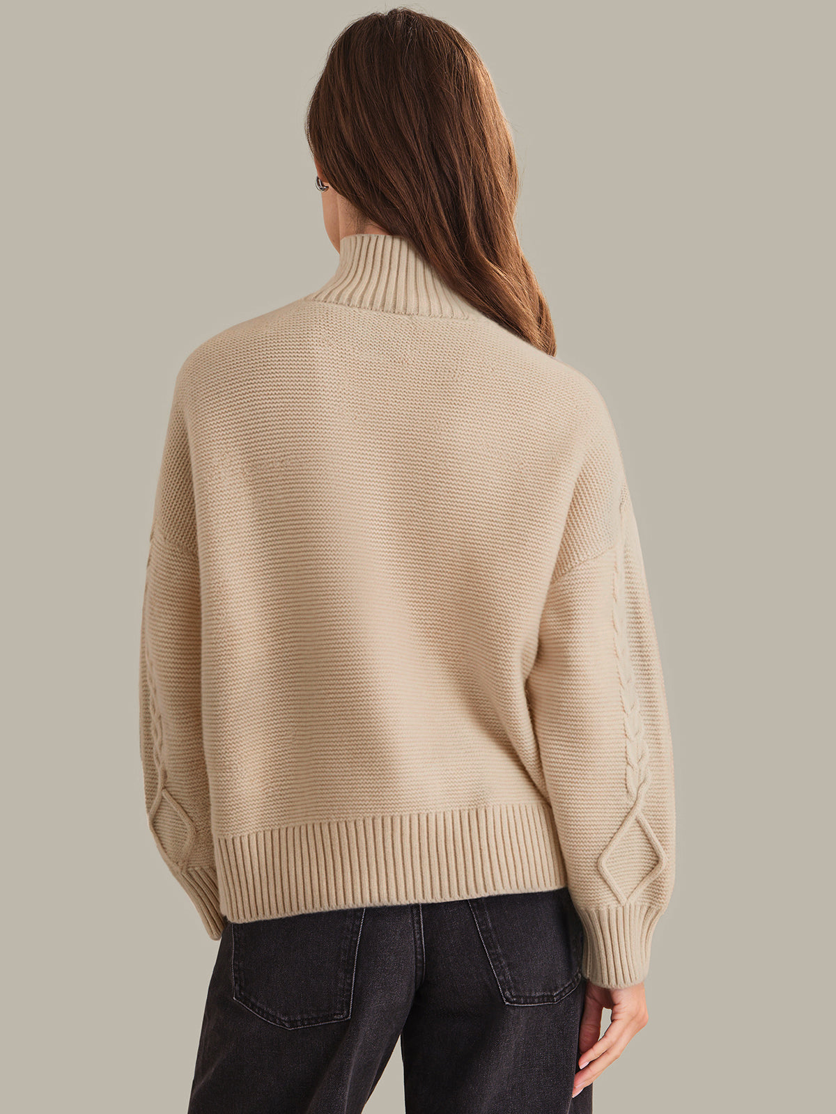 Person wearing a beige sweater on a plain background
