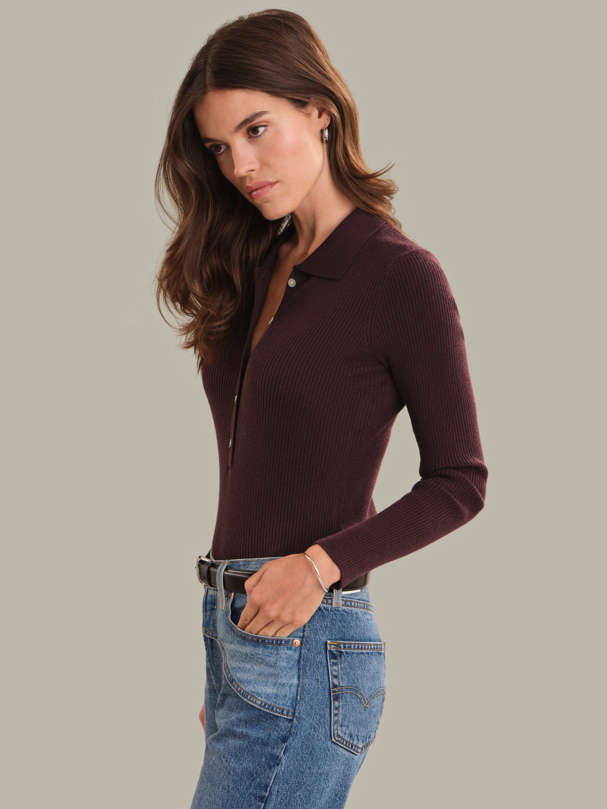 Woman wearing a wine red long-sleeve polo shirt and blue jeans on a gray background
