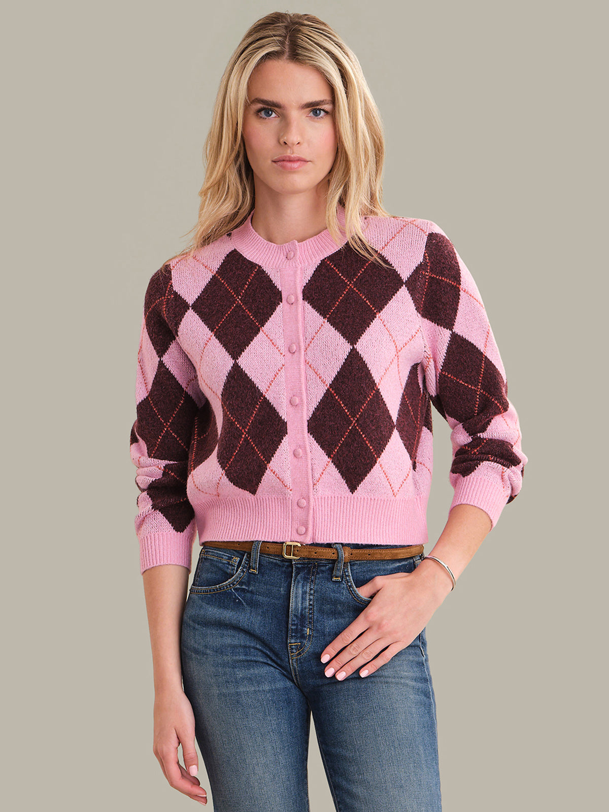 Woman wearing a pink argyle sweater and blue jeans against a gray background