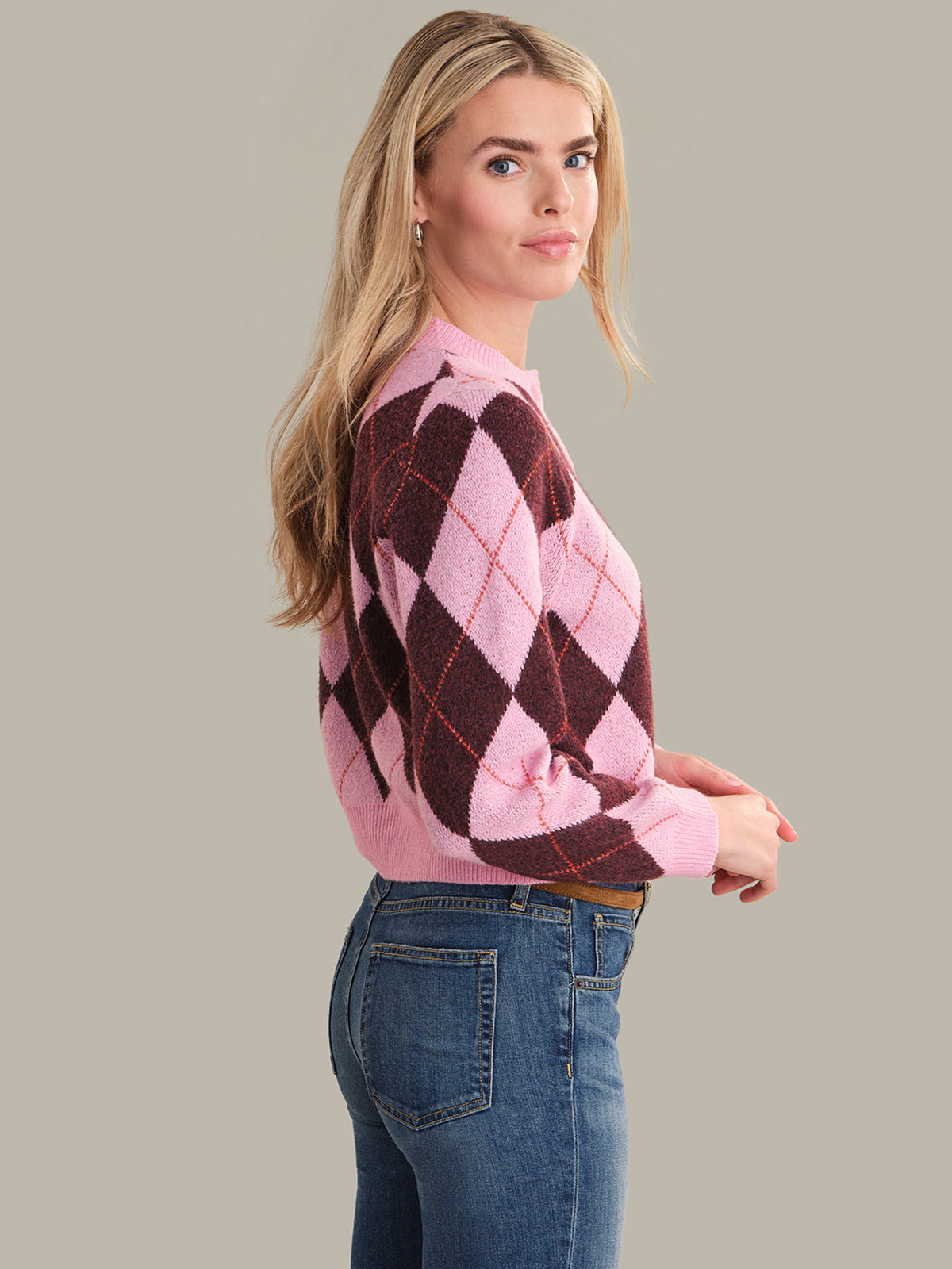 Woman wearing a pink and brown argyle sweater with blue jeans on a gray background