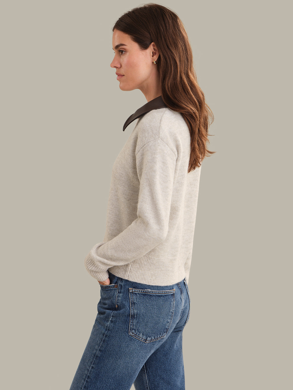 Woman wearing a light beige cardigan and blue jeans on a plain background