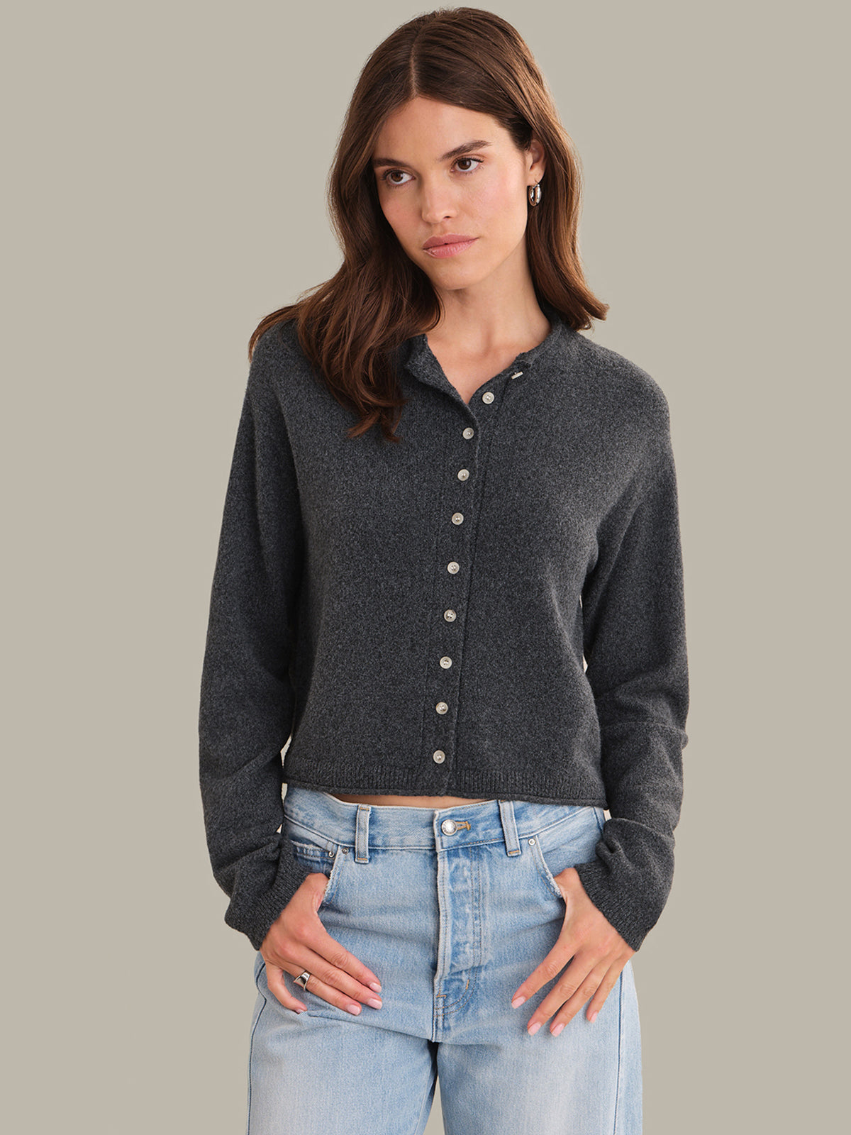 Woman wearing a dark gray button-up shirt and light blue jeans against a neutral background