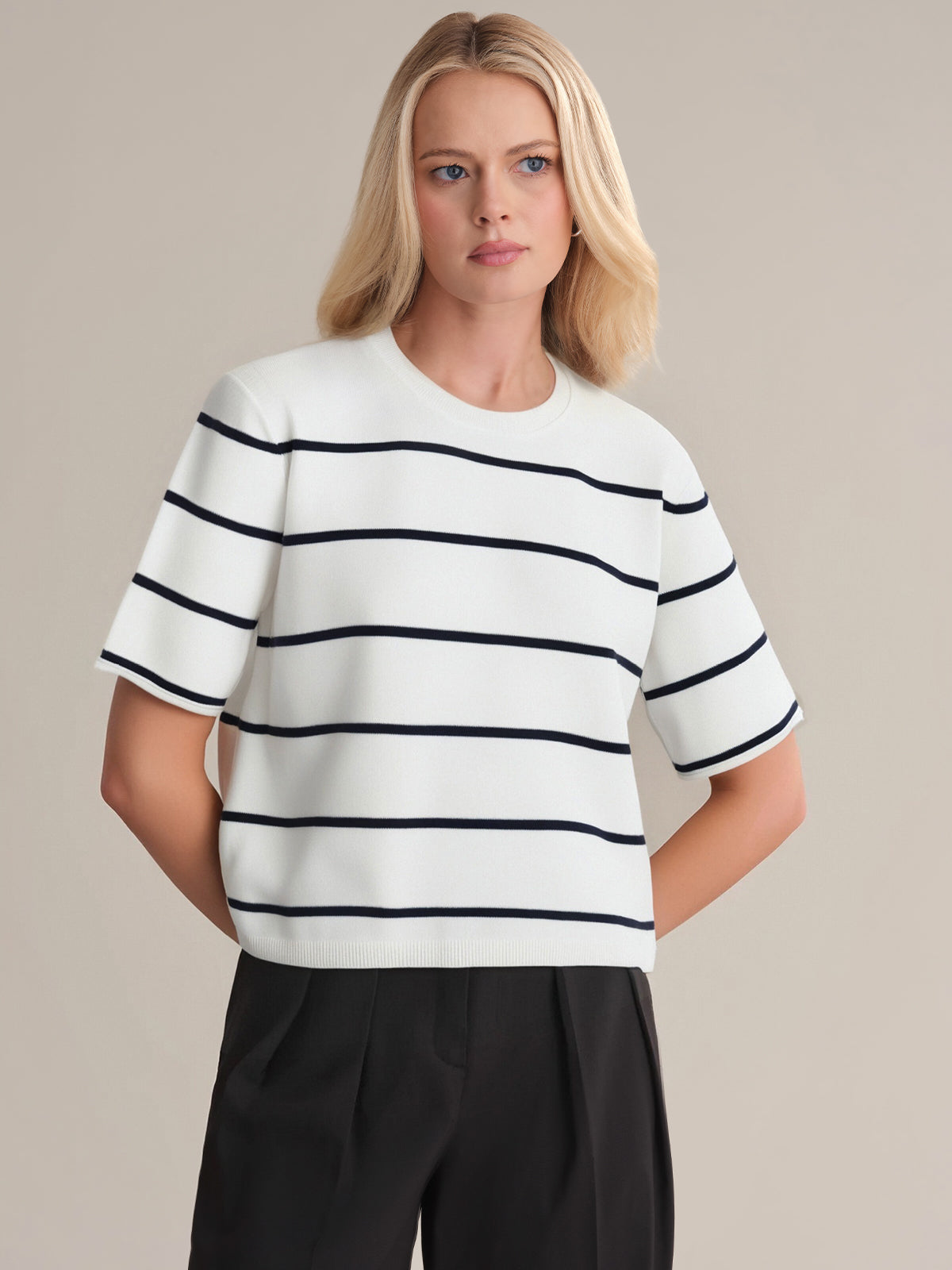 A person with straight blonde hair models a 525 America premium cotton short-sleeve top featuring black horizontal stripes, paired with black pants, against a plain light background.