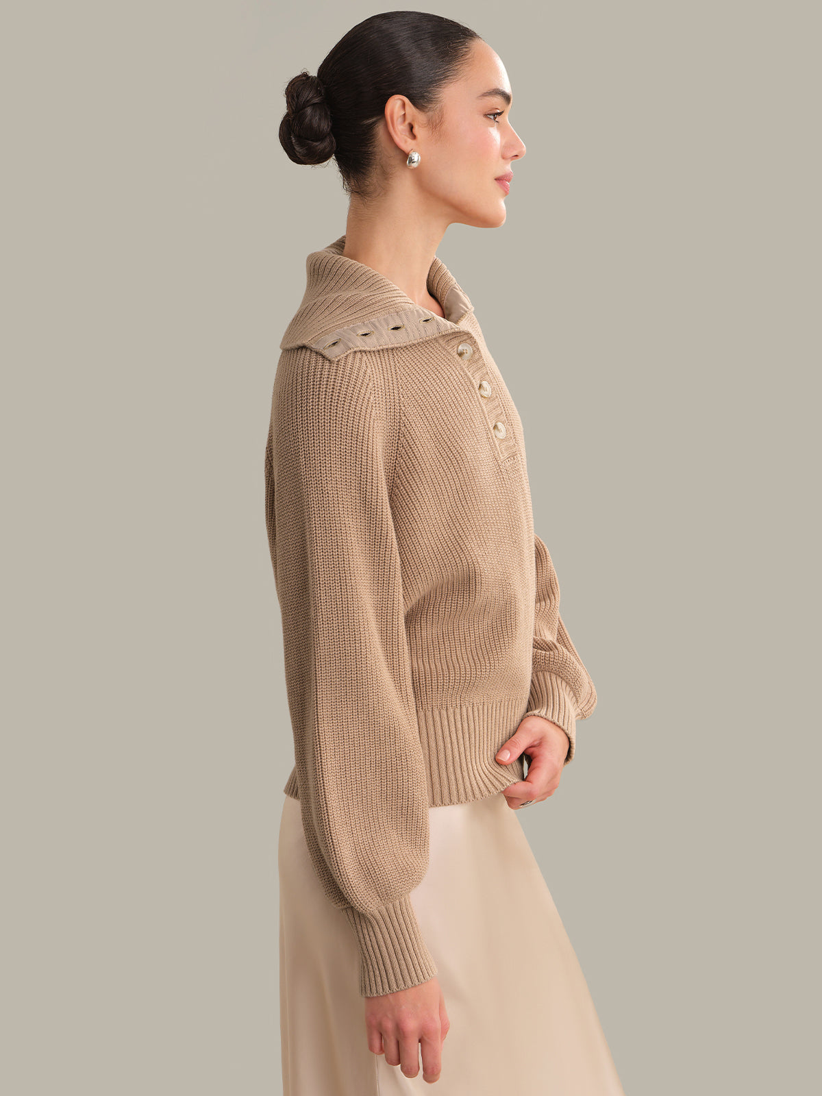 Woman wearing a beige knitted sweater with decorative collar against a neutral background